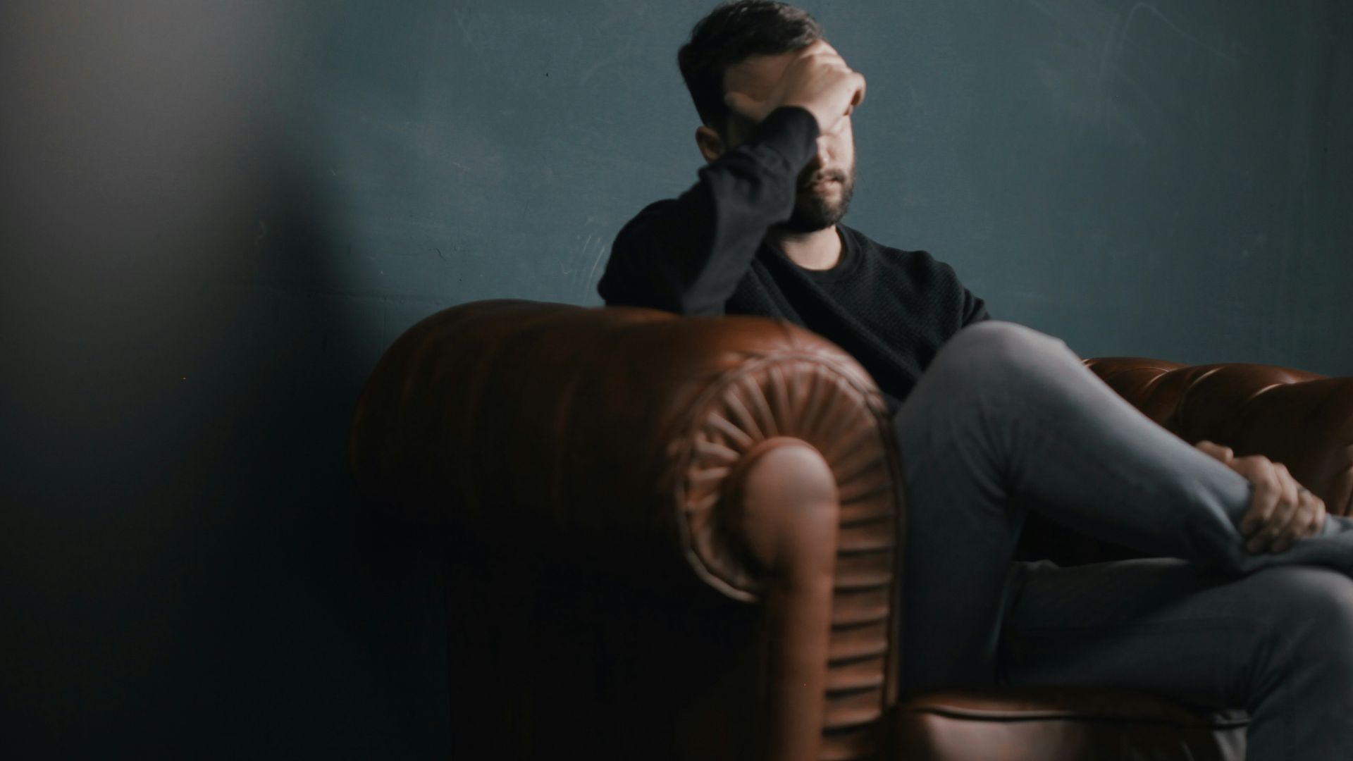 a man holds his head while sitting on a sofa