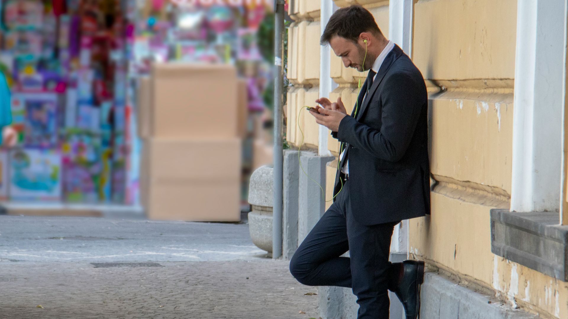 man holding his phone while leaning on building