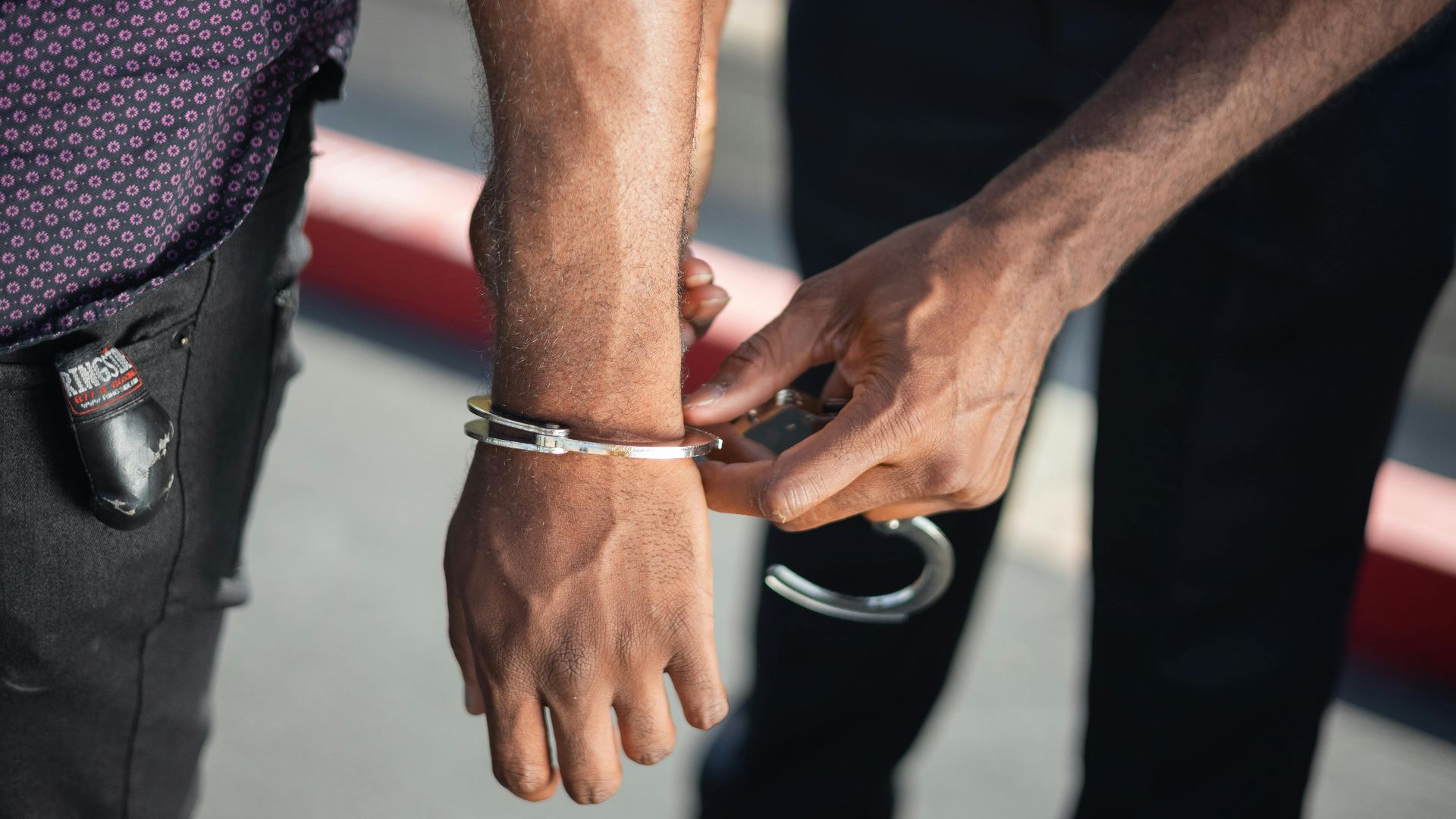 Close-up of a police officer handcuffing a suspect outdoors, enforcing law.
