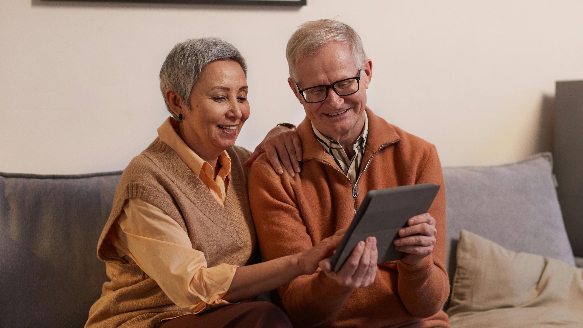 Happy senior couple sitting together on a sofa using a tablet indoors.