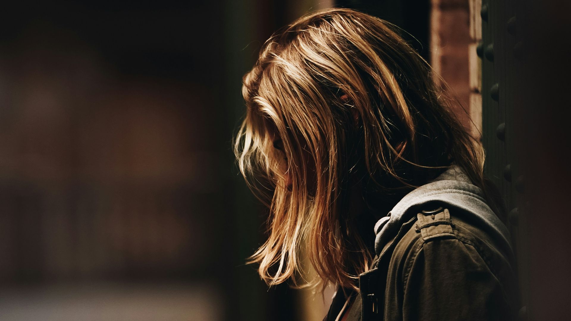 woman leaning against a wall in dim hallway