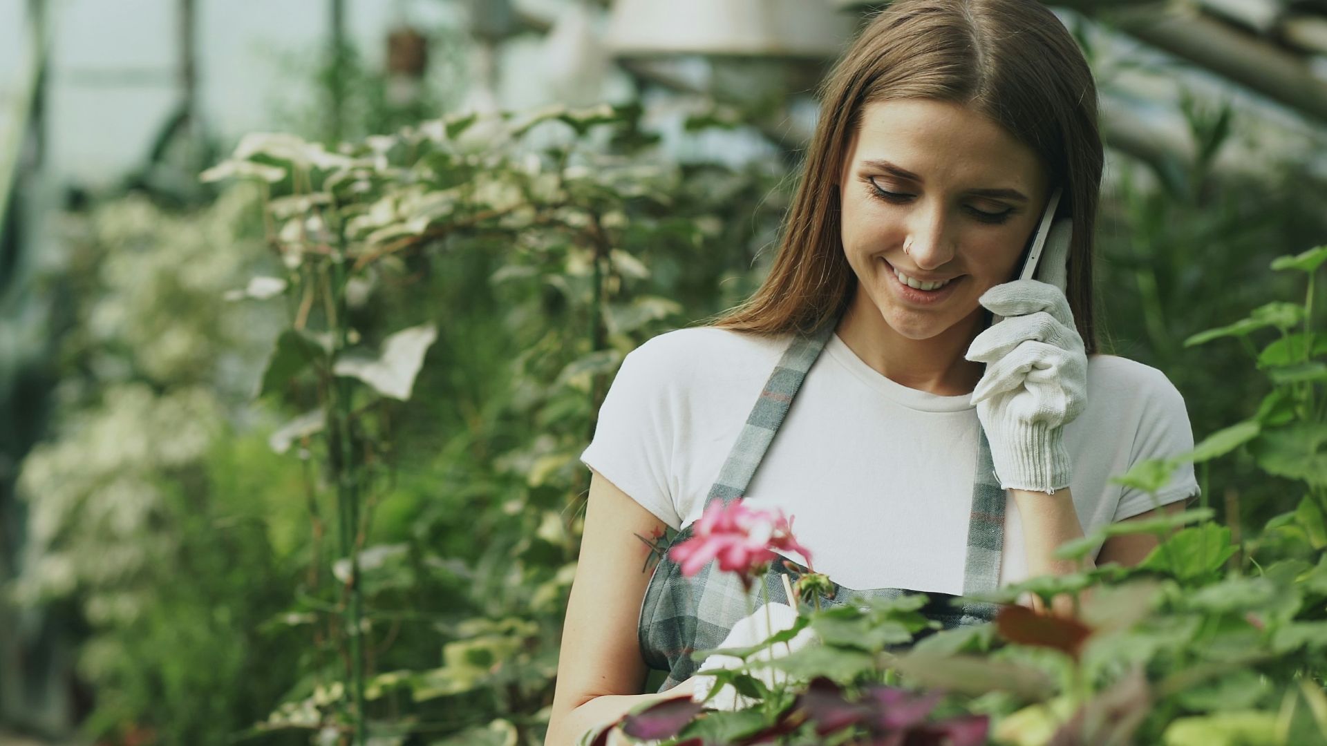 Woman talking on phone in greenhouse with plants