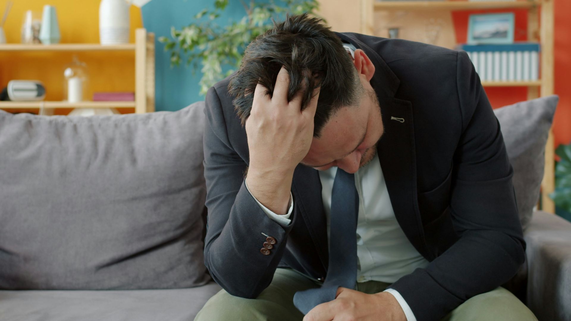 Man in suit sitting on couch with head in hands.