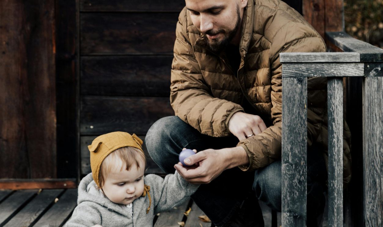 Man in Brown Jacket and Blue Denim Jeans Sitting Holding His Child