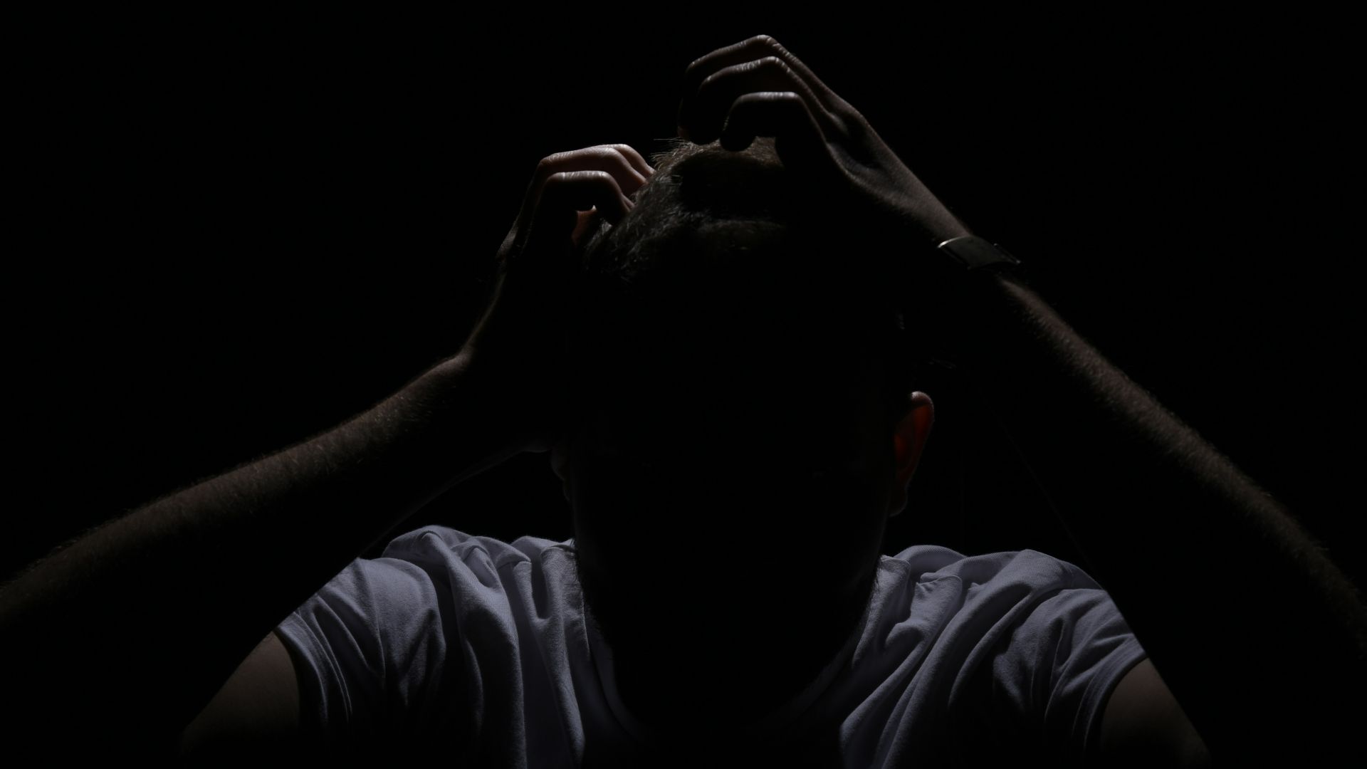 a man in the dark covering his face with his hands