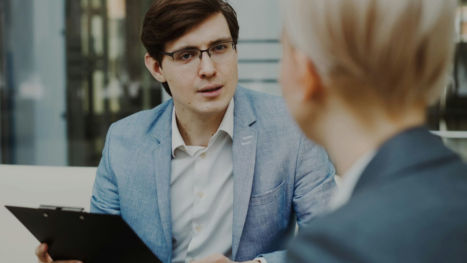 Man in suit holding clipboard talking to woman