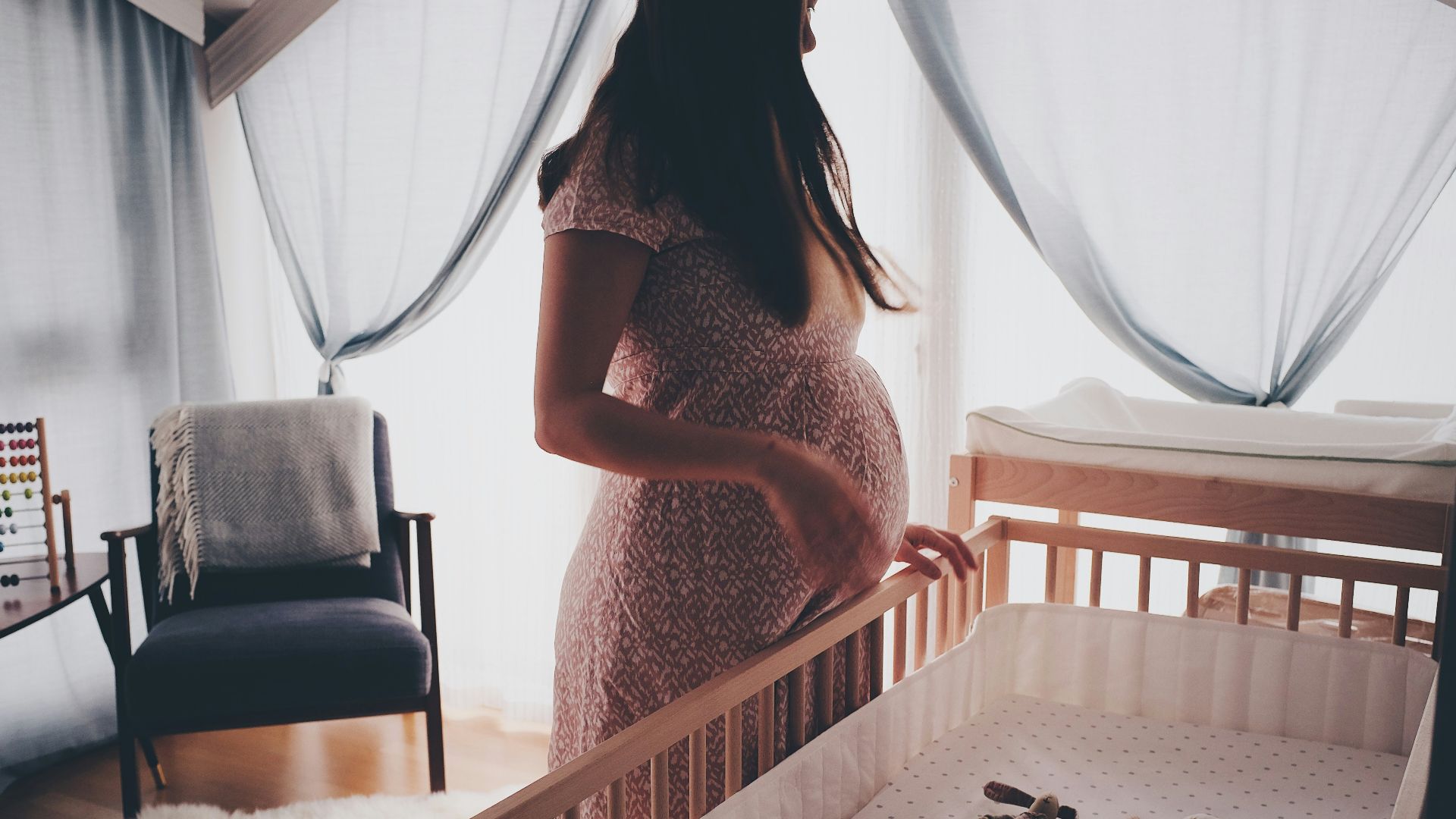 woman in white lace sleeveless dress standing beside brown wooden crib