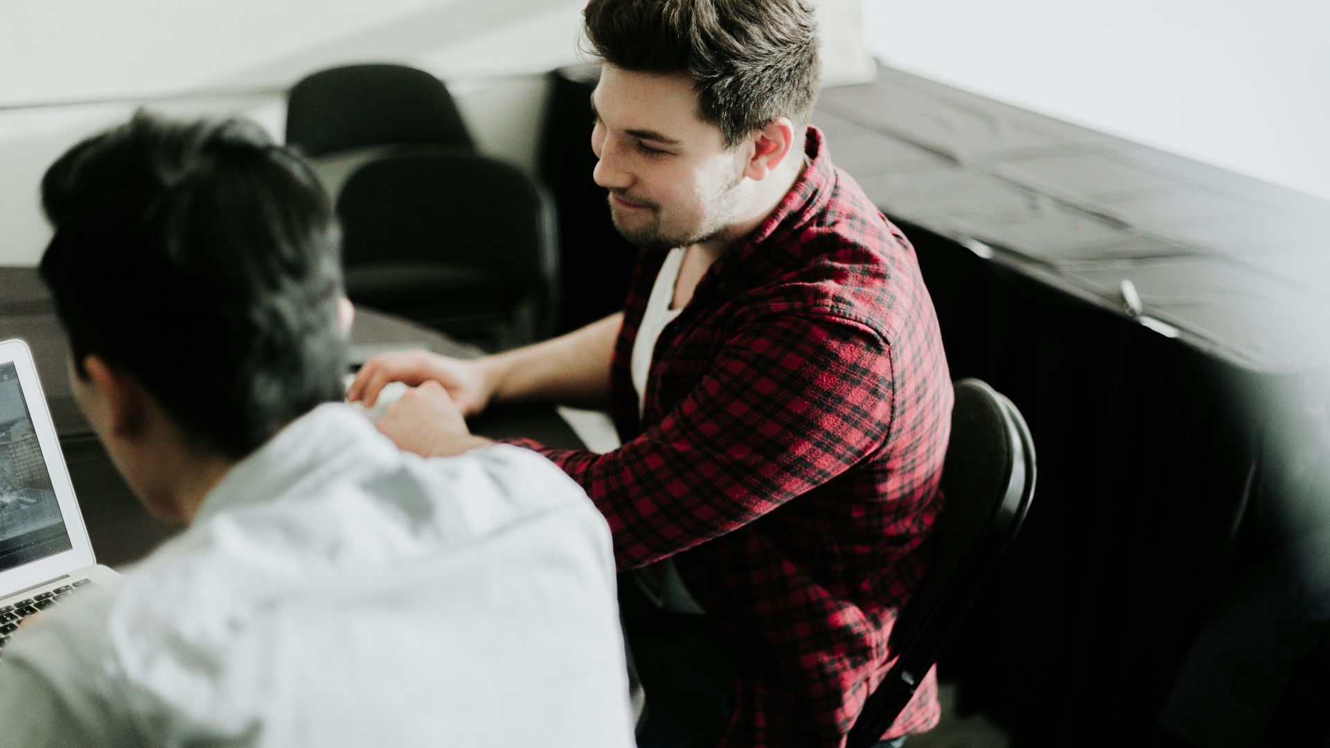 a man sitting at a desk shaking hands with another man
