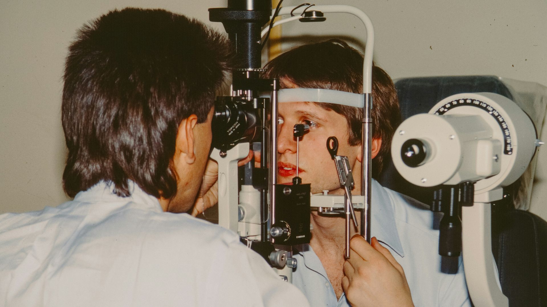 Optometrist examining a patient's eye with equipment.