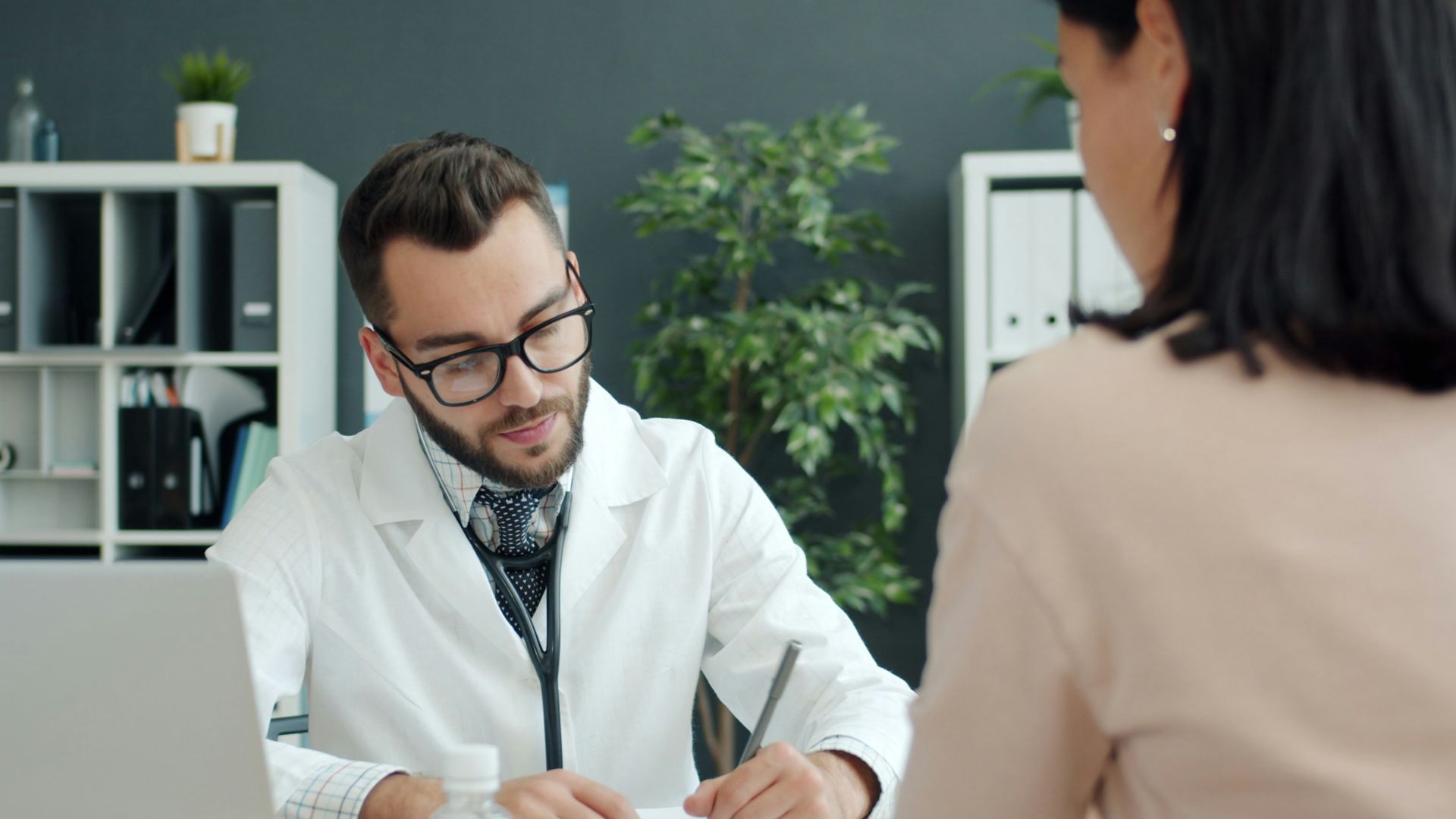 Doctor writing notes while patient sits opposite.