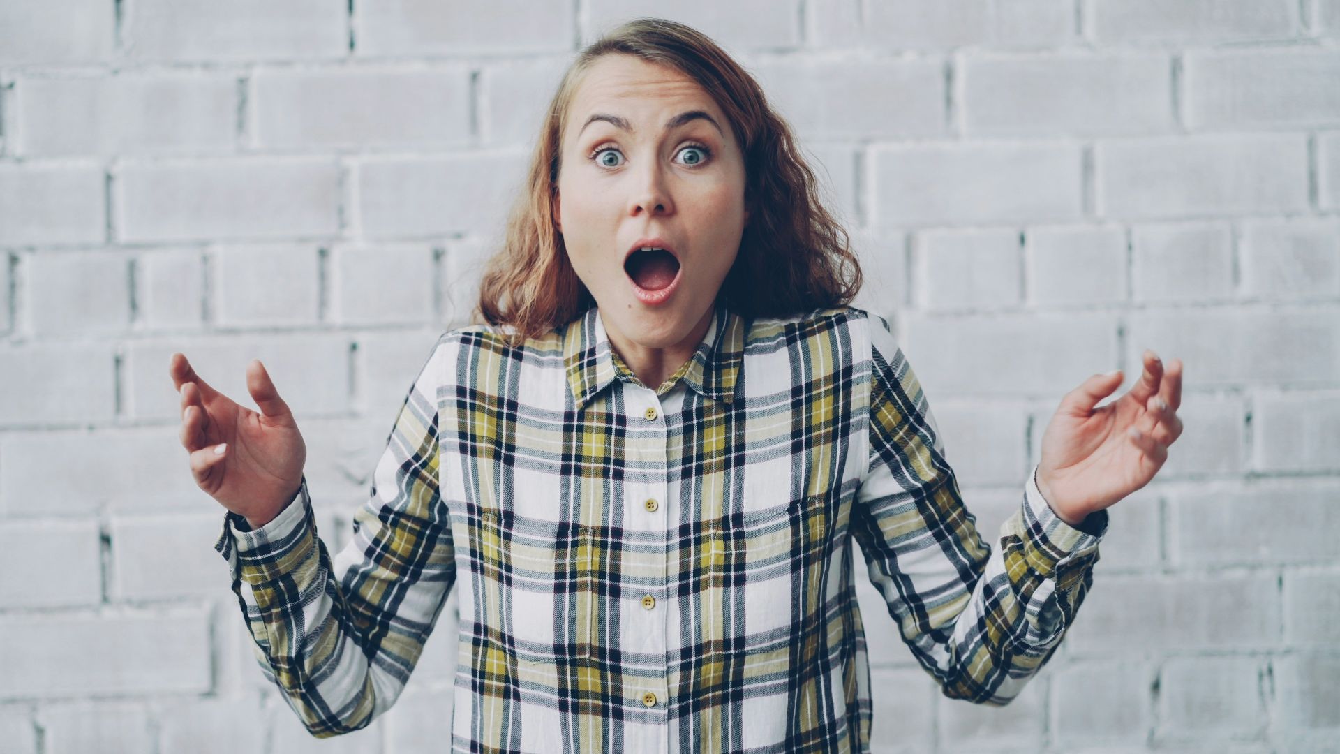 Young woman with surprised expression against brick wall