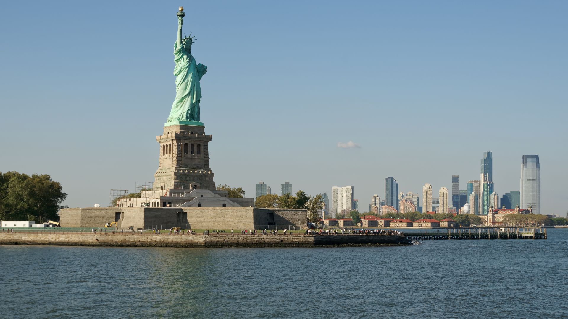 View of Liberty Island from the ferry to Lower Manhattan. Ellis Island and Jersey City on the right