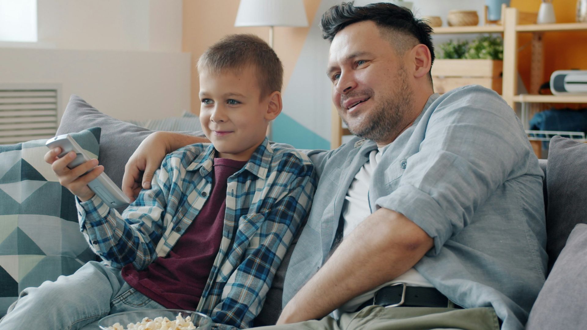 Father and son watching television together on couch.