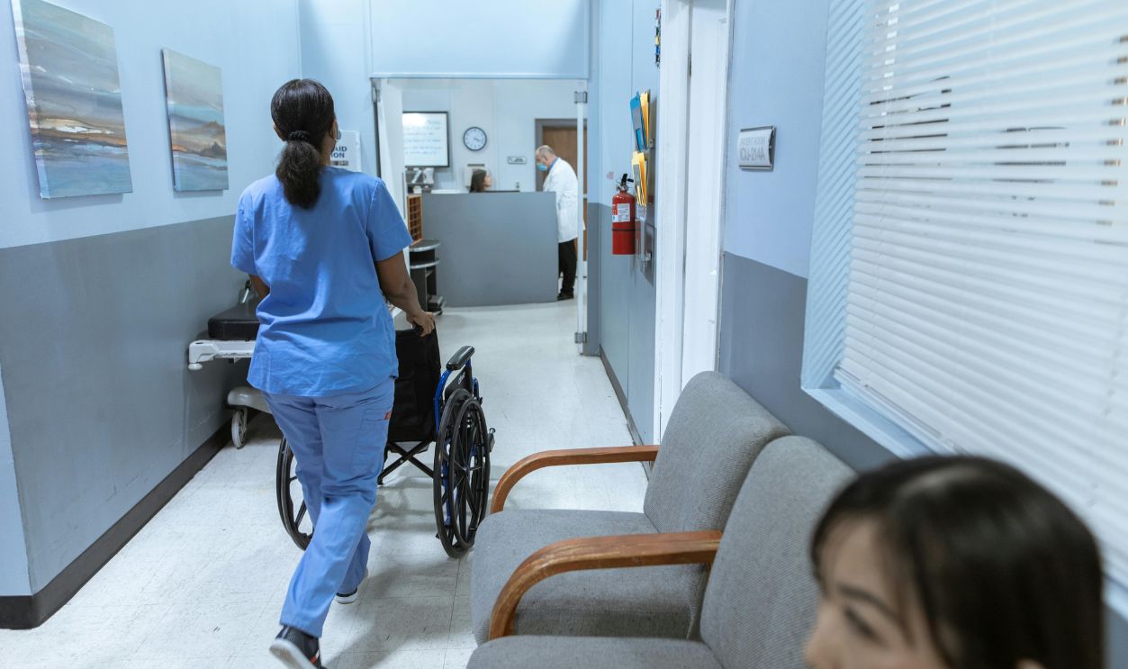 Nurse Pushing a Wheelchair on Hospital Hallway