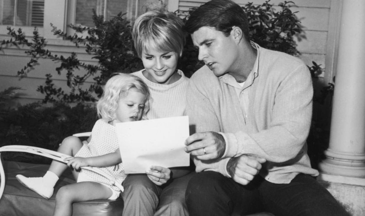 American actor and rock n' roll singer Rick Nelson (1940-1985) sits outdoors on a lawn chair with his wife Kristin Harmon 	