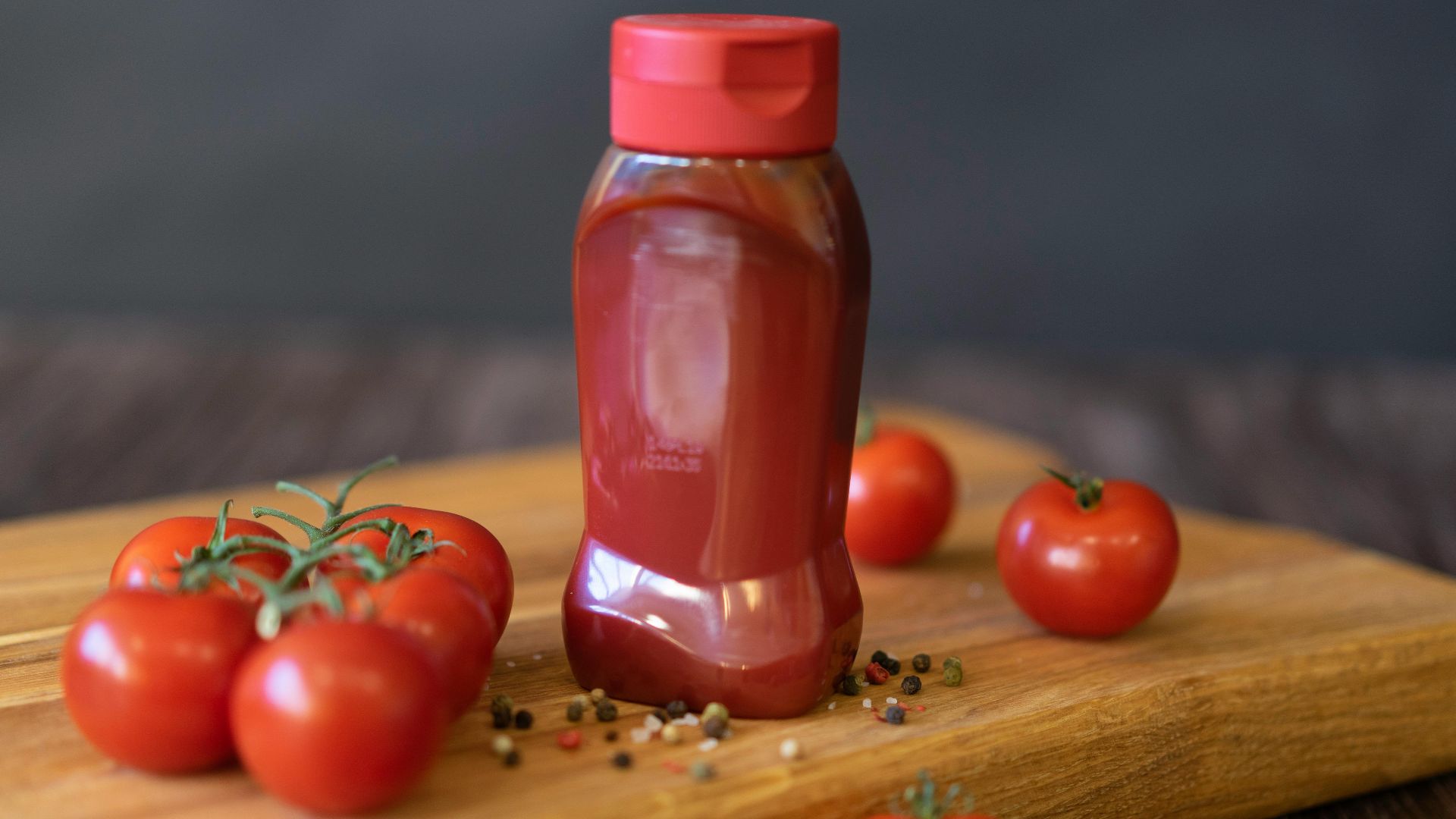Close-up of tomatoes and ketchup bottle on a wooden board with peppercorns.