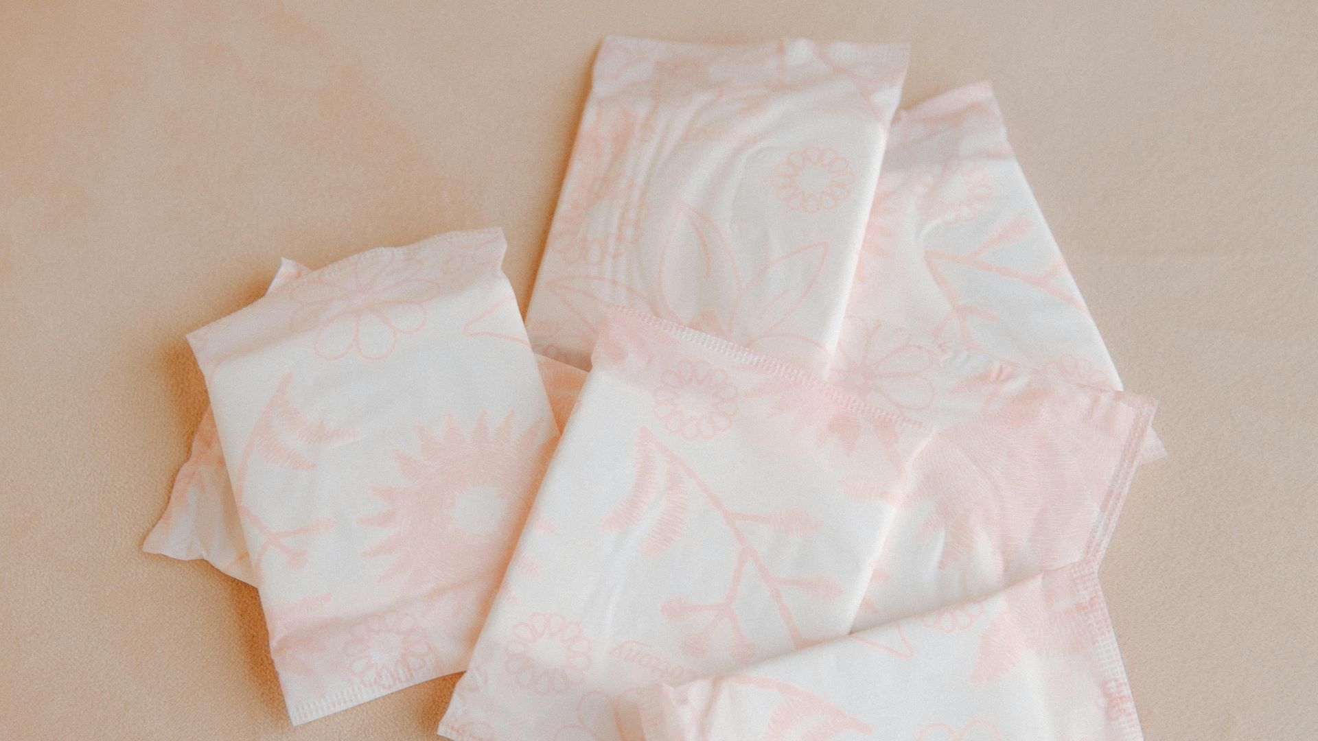 Variety of sanitary pads arranged on a soft beige surface for feminine hygiene.