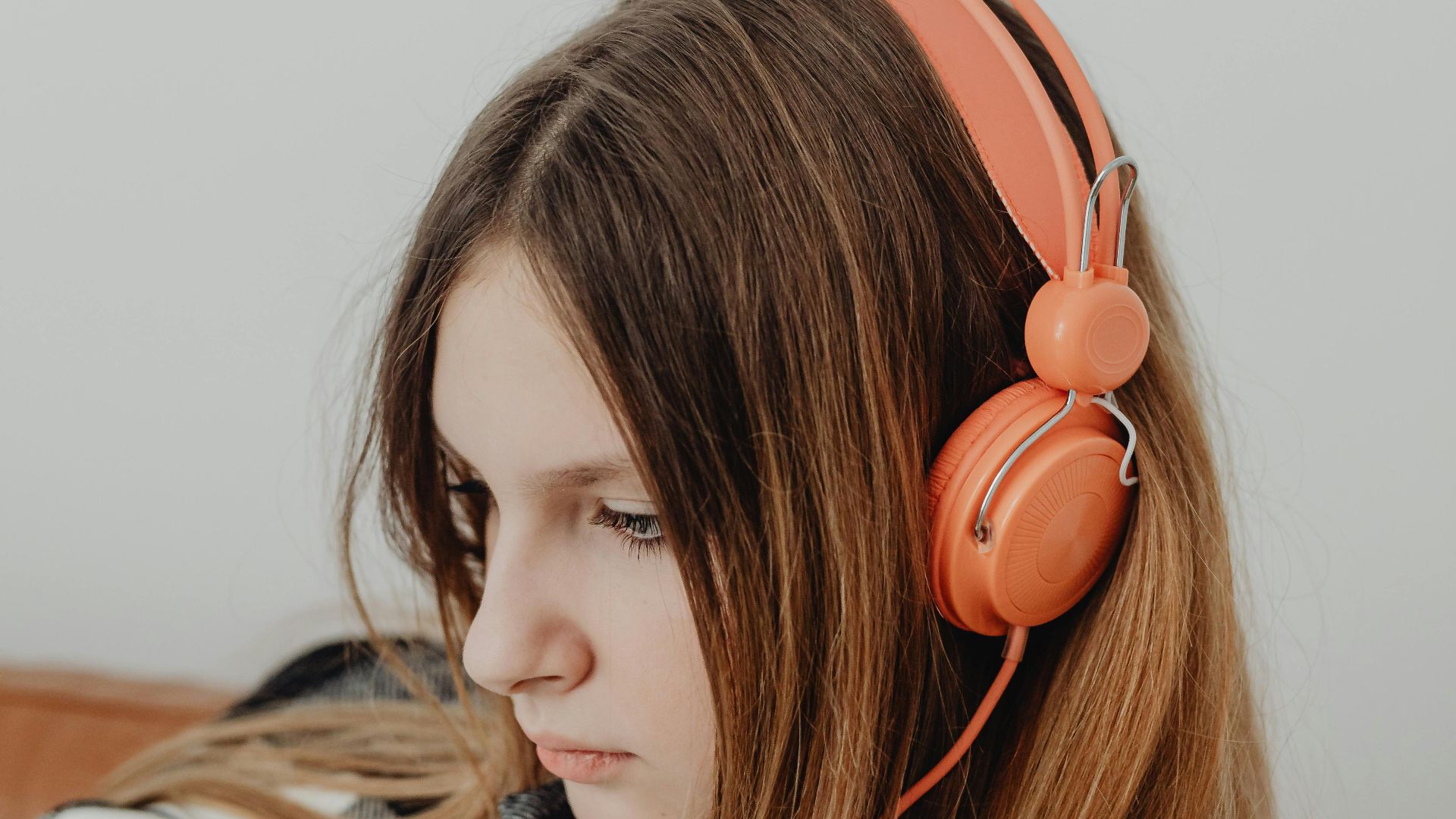 Portrait of a young woman with long blonde hair wearing orange headphones indoors.