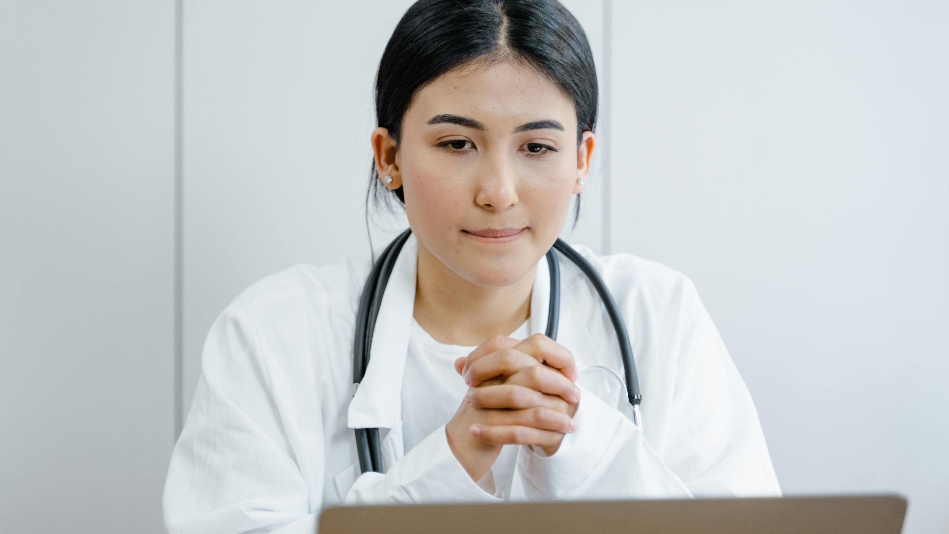 Young female doctor in white coat consulting online with stethoscope indoors.