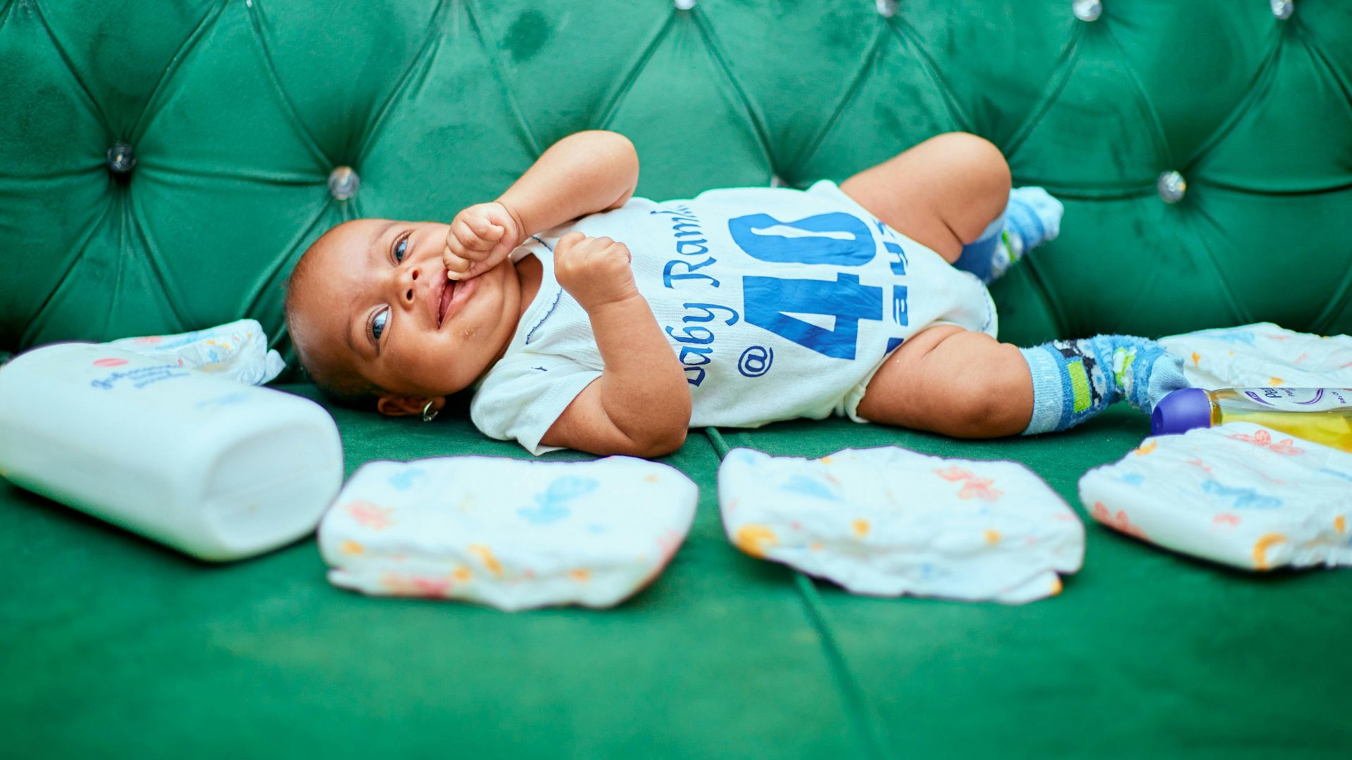 Adorable baby lying on a green sofa with diapers, showcasing a cute smile and playful demeanor.