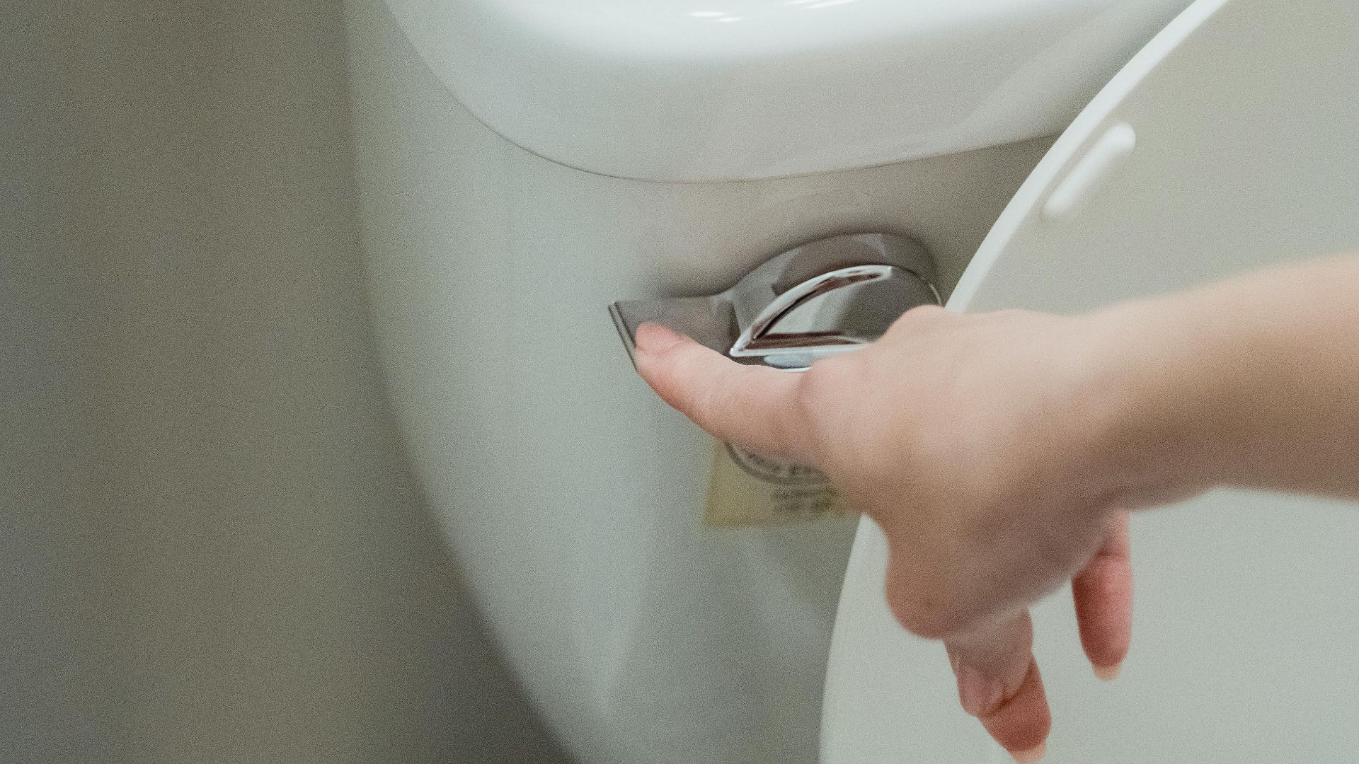 Close-up of a hand flushing a modern toilet, emphasizing hygiene and water conservation.