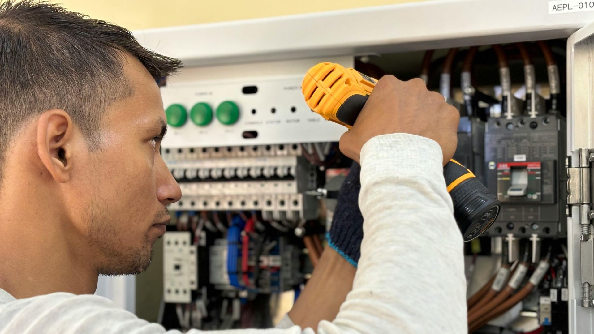 Professional electrician using a drill on an indoor circuit breaker panel.