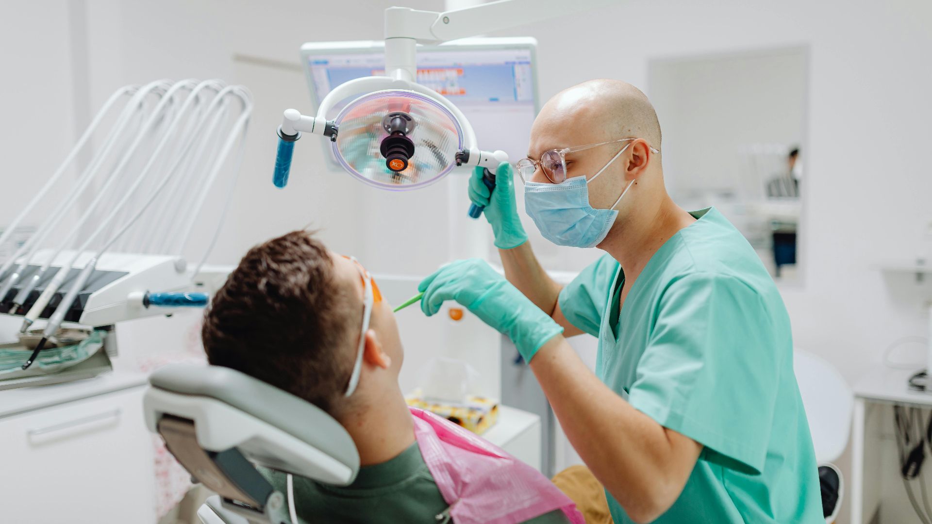 A dentist in a medical clinic conducts a dental check-up on a seated patient.