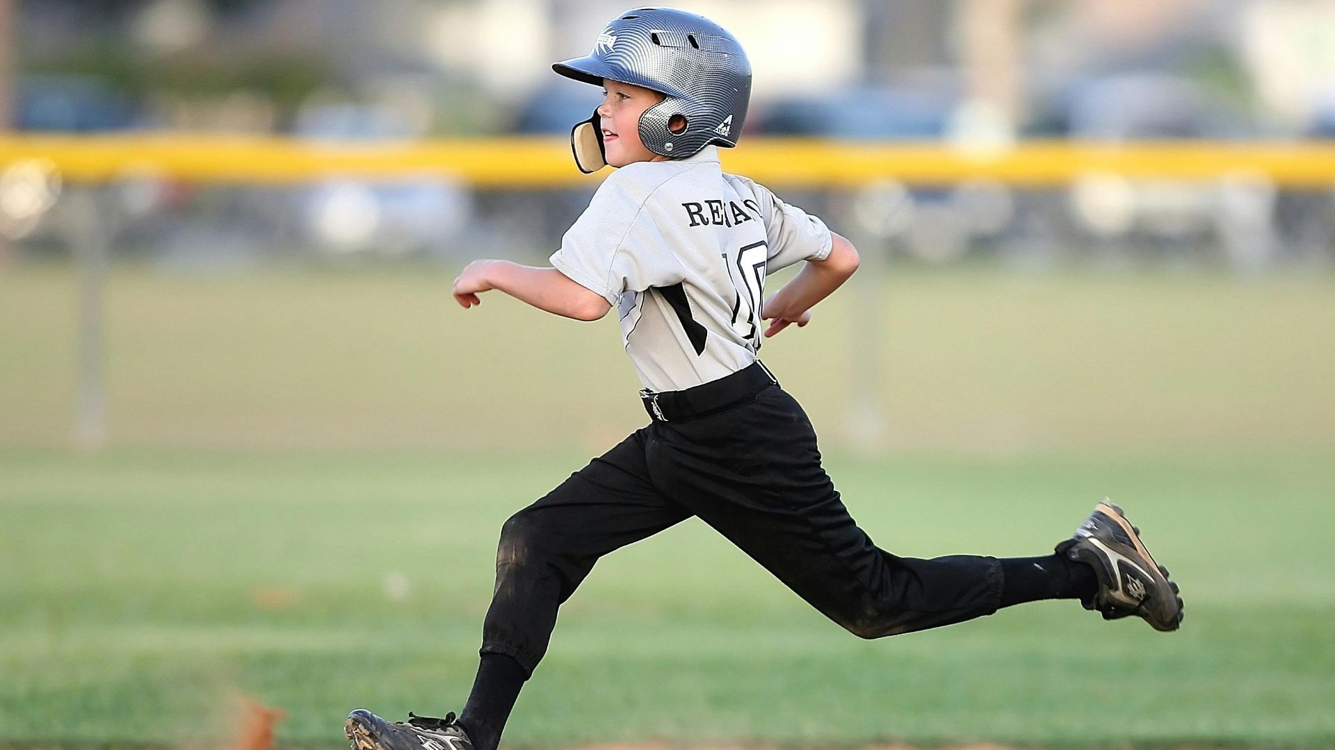 Action shot of a young baseball player running fast on the field, wearing uniform and helmet.