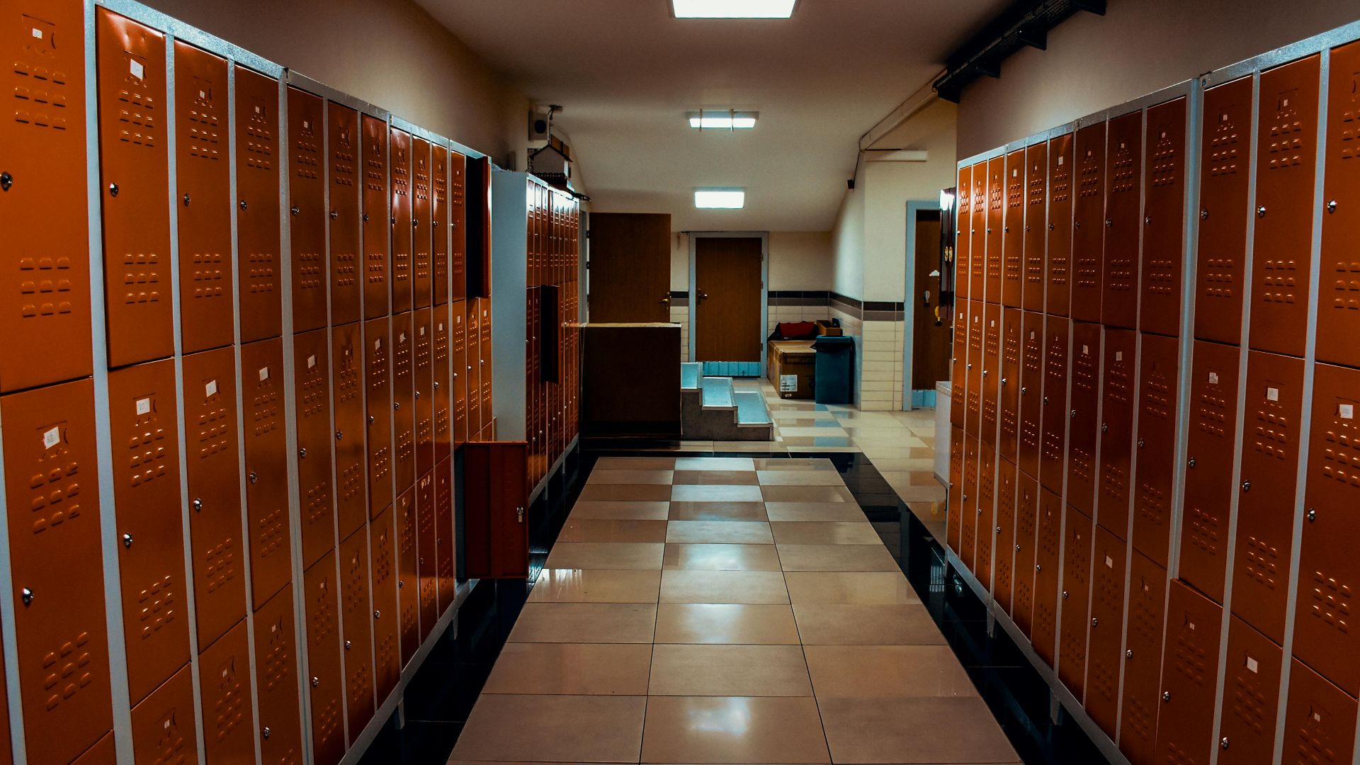 Vacant locker room with orange lockers and tiled flooring in a modern sports facility.