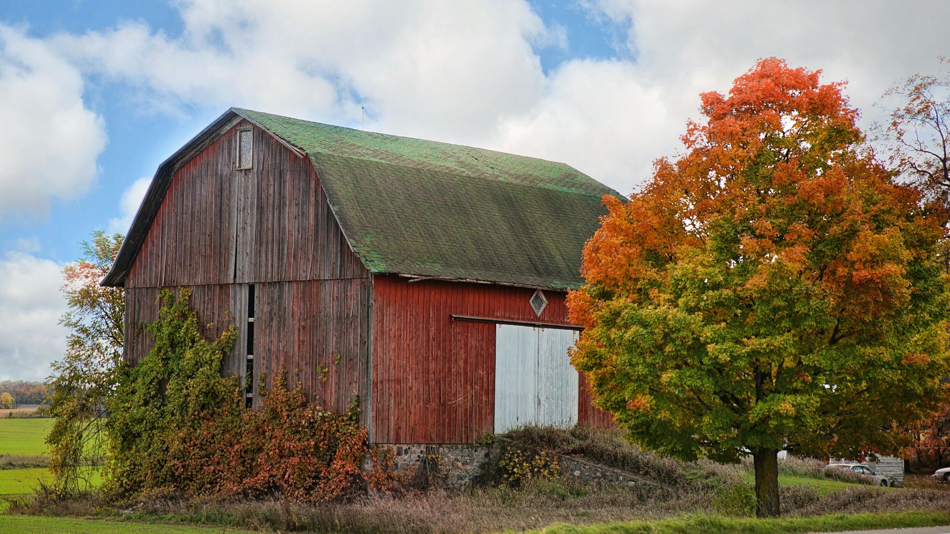Charming red barn surrounded by autumn foliage under a bright sky.