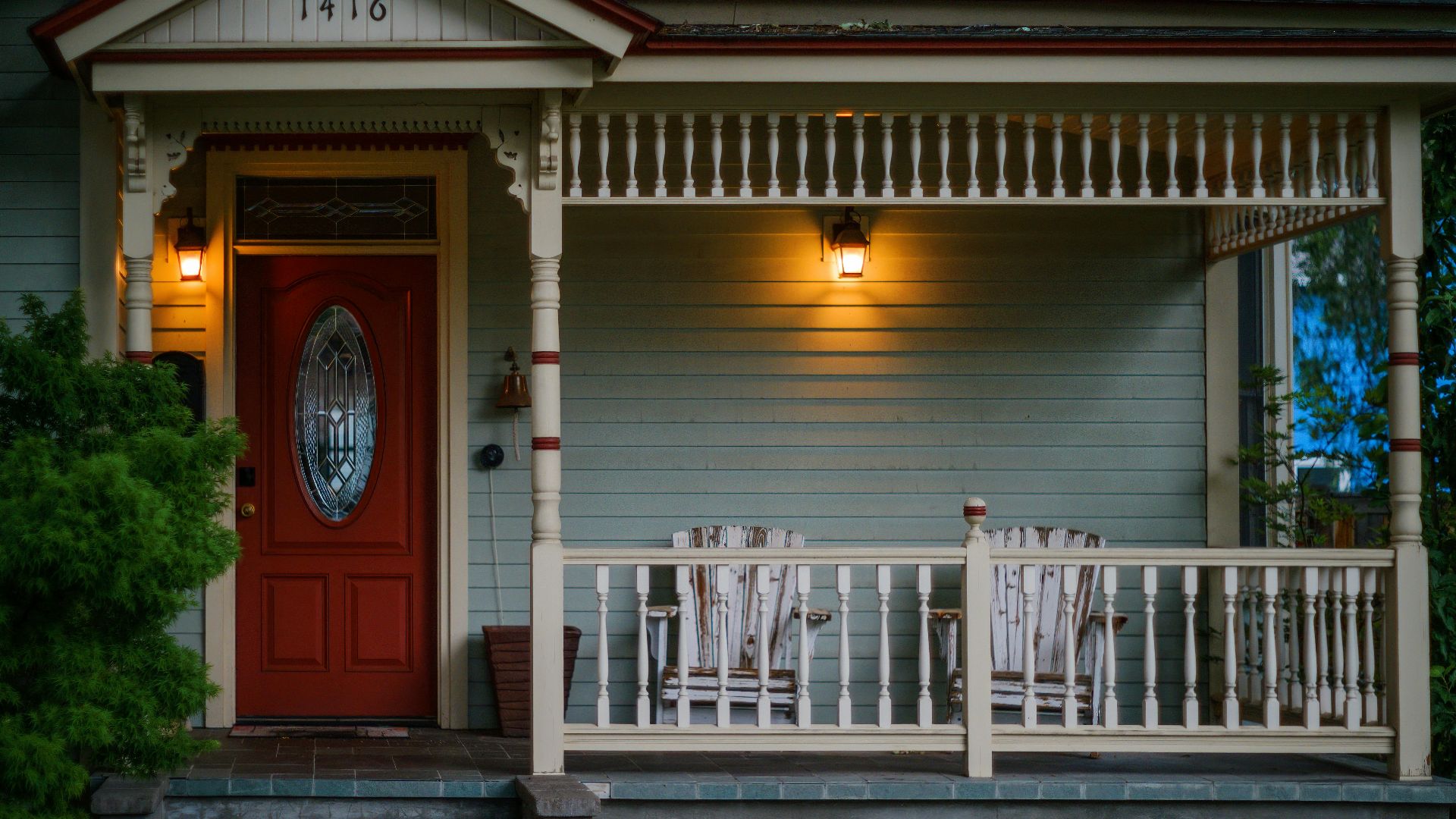 Inviting porch with red door, wooden armchairs, and glowing lights, perfect for evening relaxation.