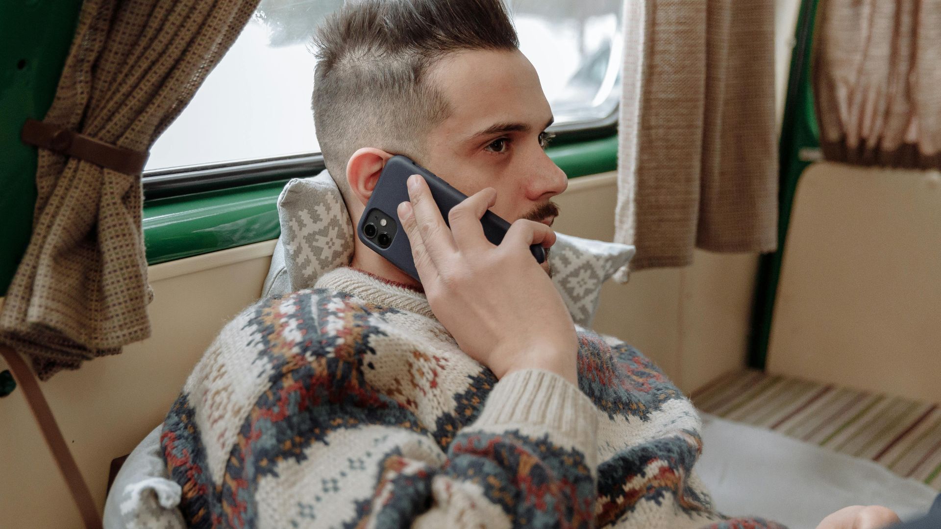 Casual adult man wearing sweater, relaxing indoors while talking on phone.