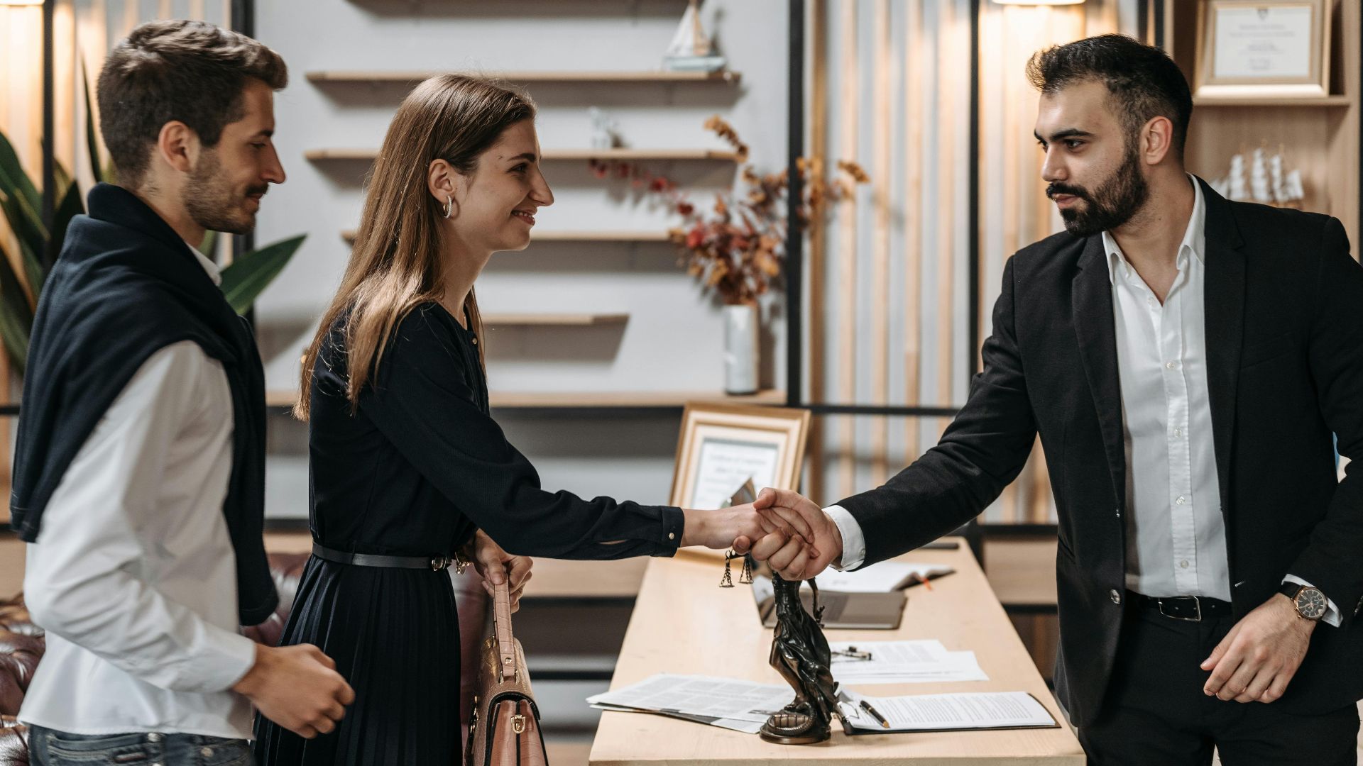 A professional meeting in a modern office with a couple shaking hands with a businessman.