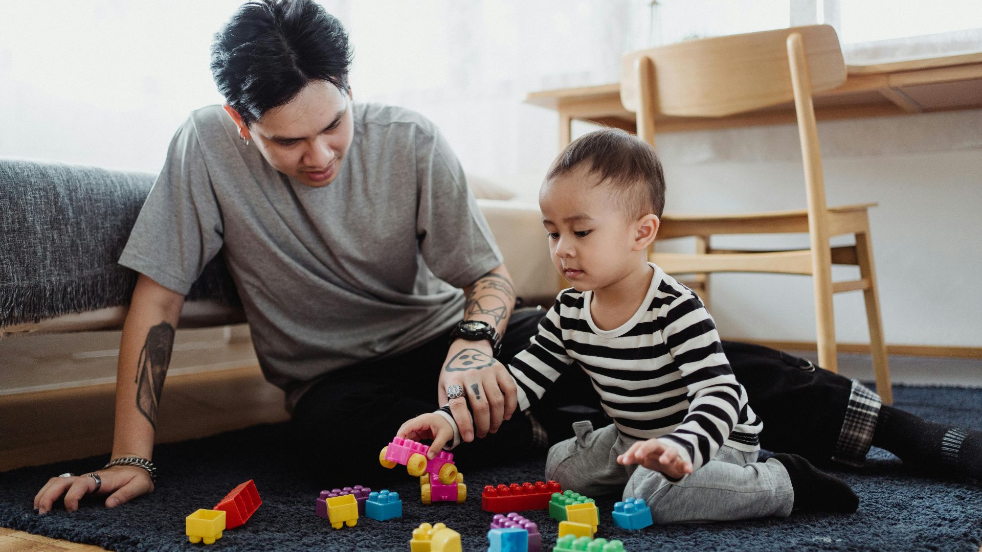 A father and son playing with colorful building blocks in a cozy indoor setting.