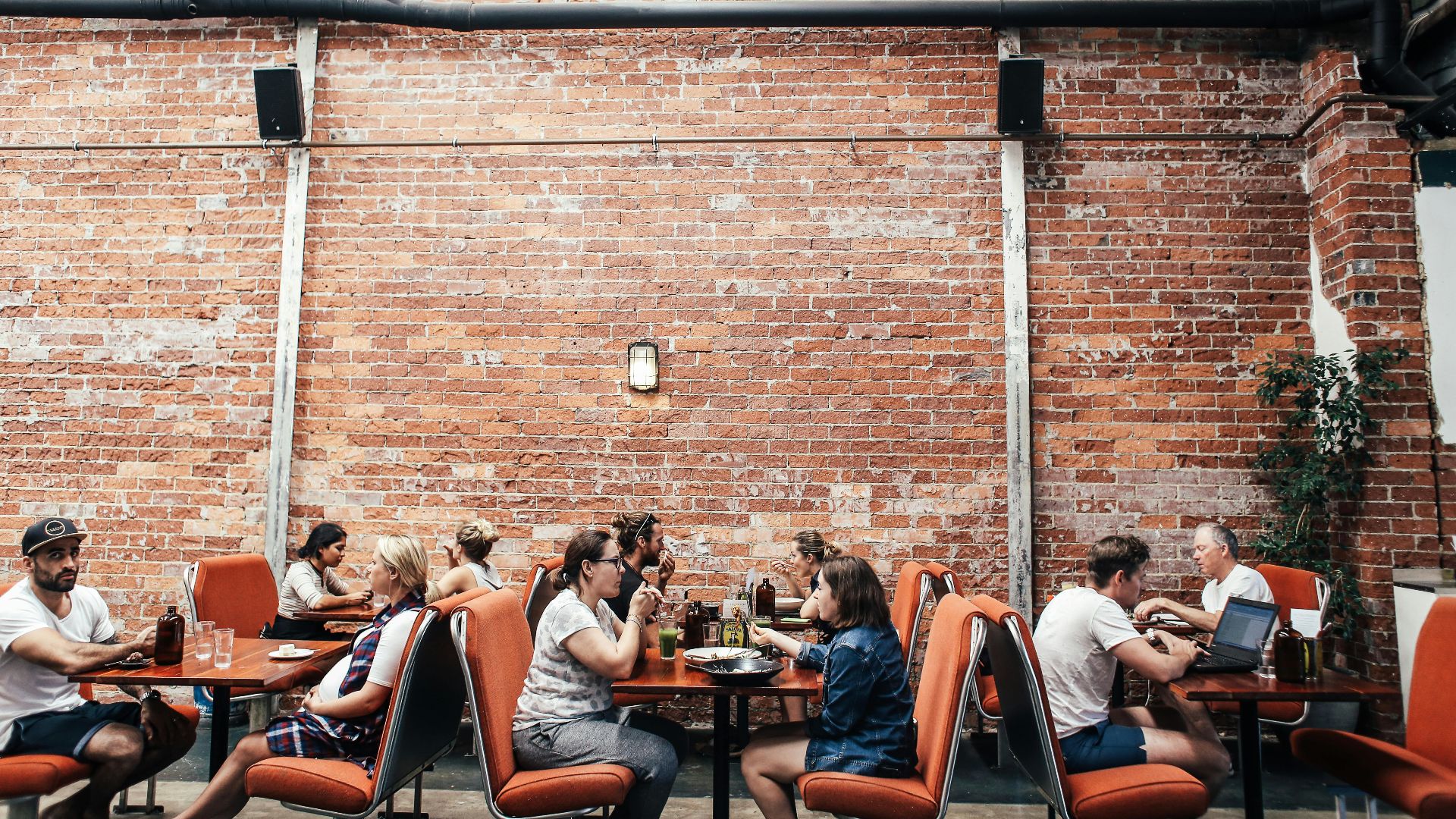 People enjoying leisure time at an outdoor restaurant, brick wall backdrop, casual atmosphere.