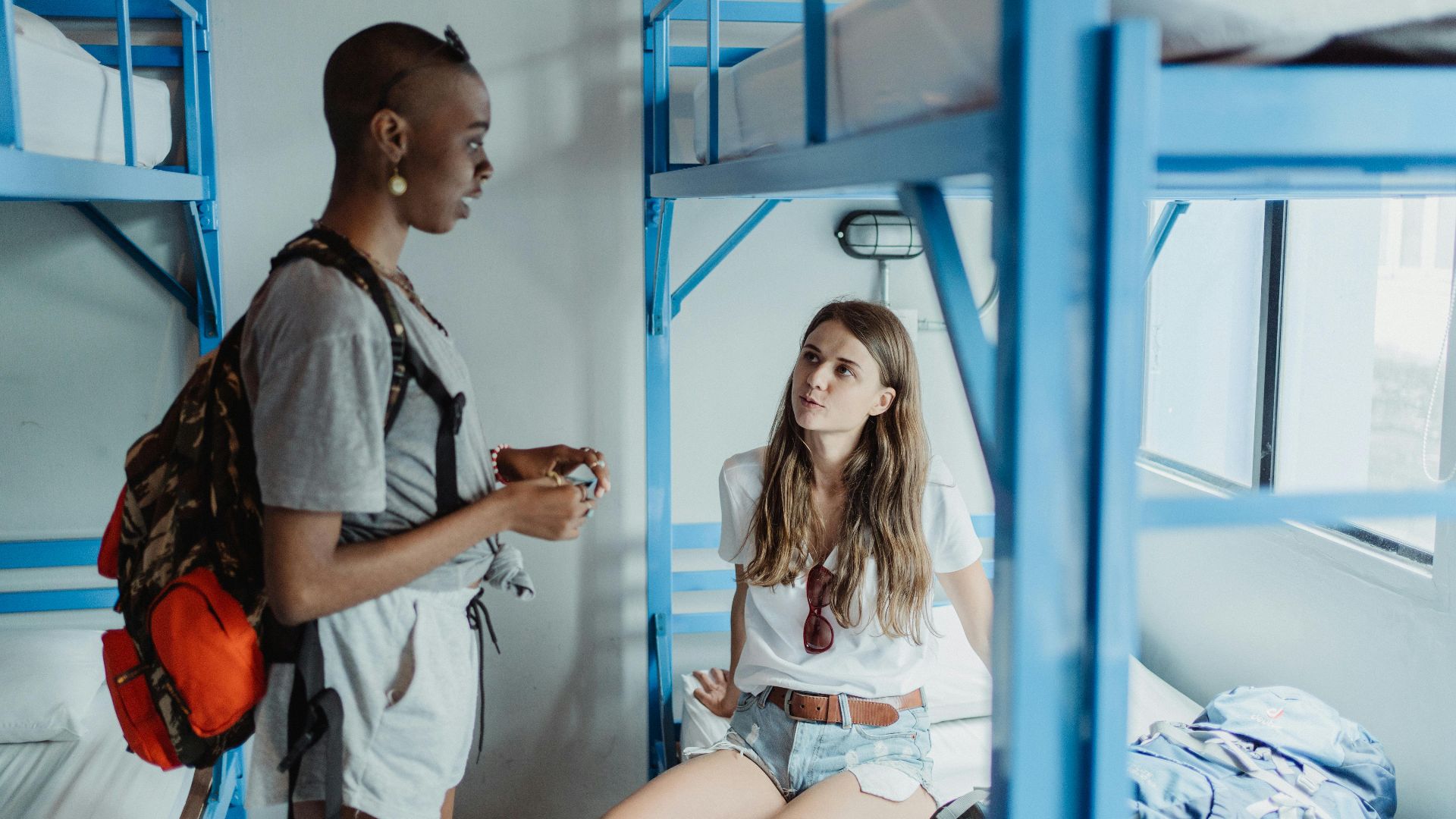 Two travelers converse in a hostel dormitory, showcasing diverse culture and adventure.