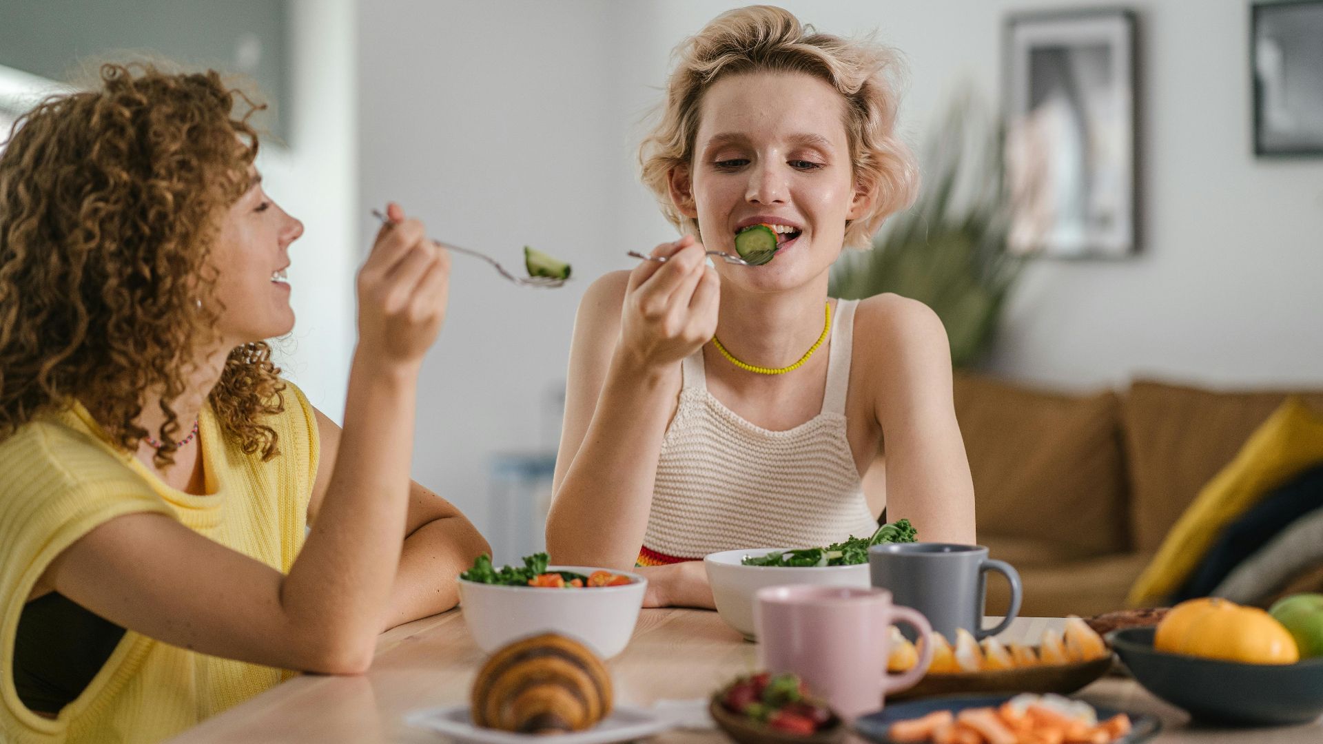 Two women enjoying a healthy meal at a cozy dining table, sharing a joyful indoor breakfast moment.