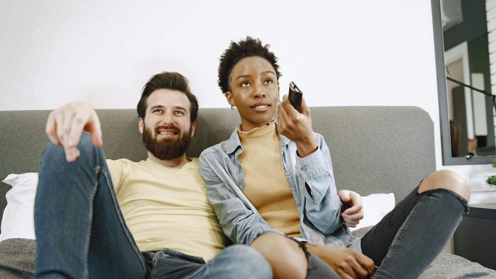 Multiracial couple enjoying a relaxing time together on a sofa, engaged in watching TV indoors.