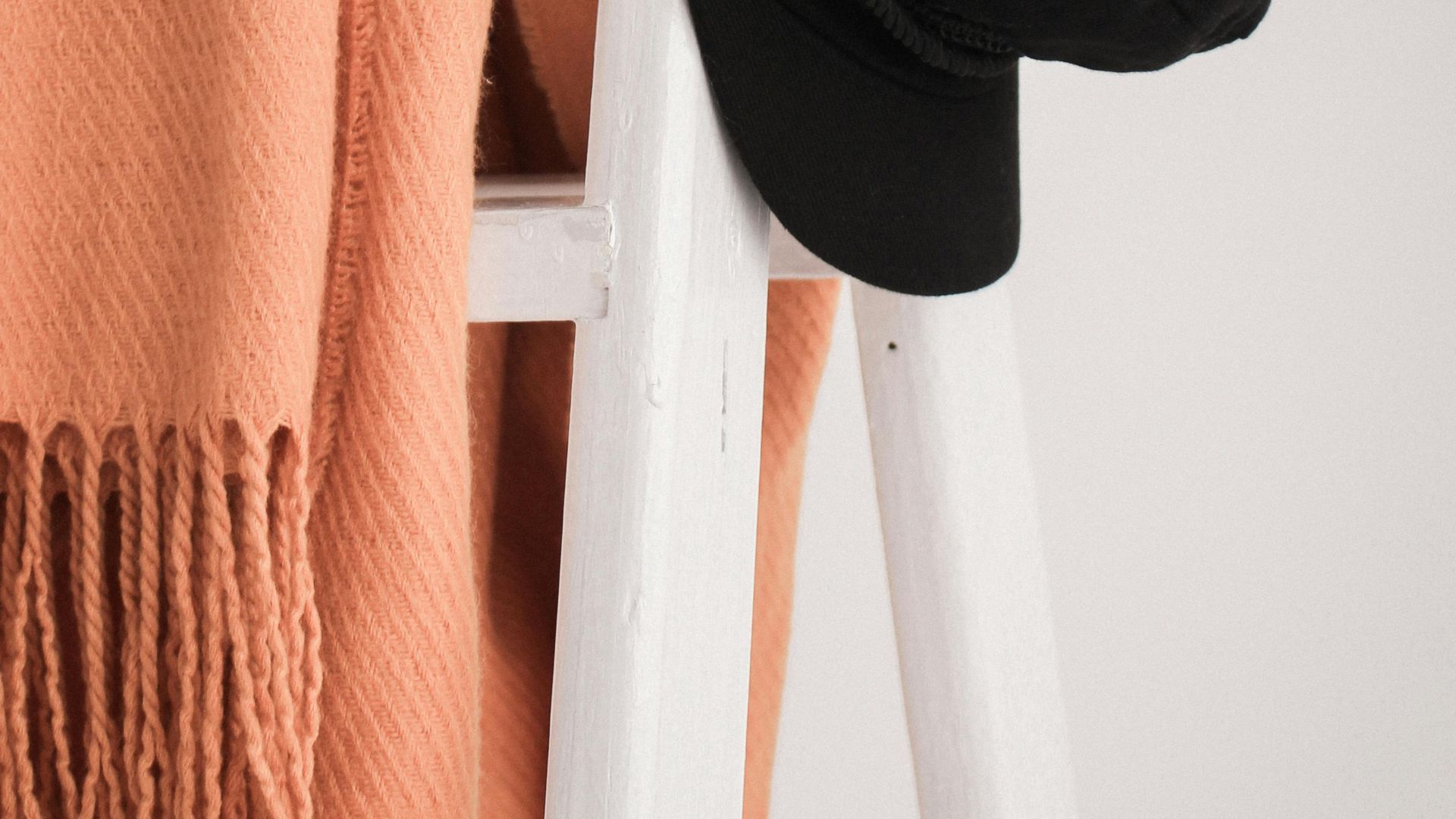 Stylish black hat and orange shawl hanging on a white ladder.