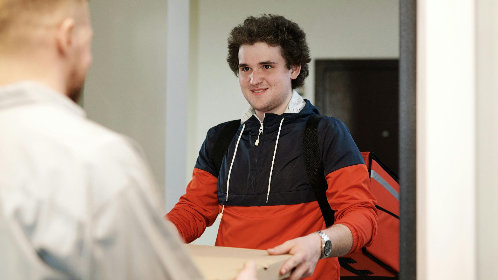 Pizza delivery man in casual wear delivers pizza box to a customer indoors, smiling