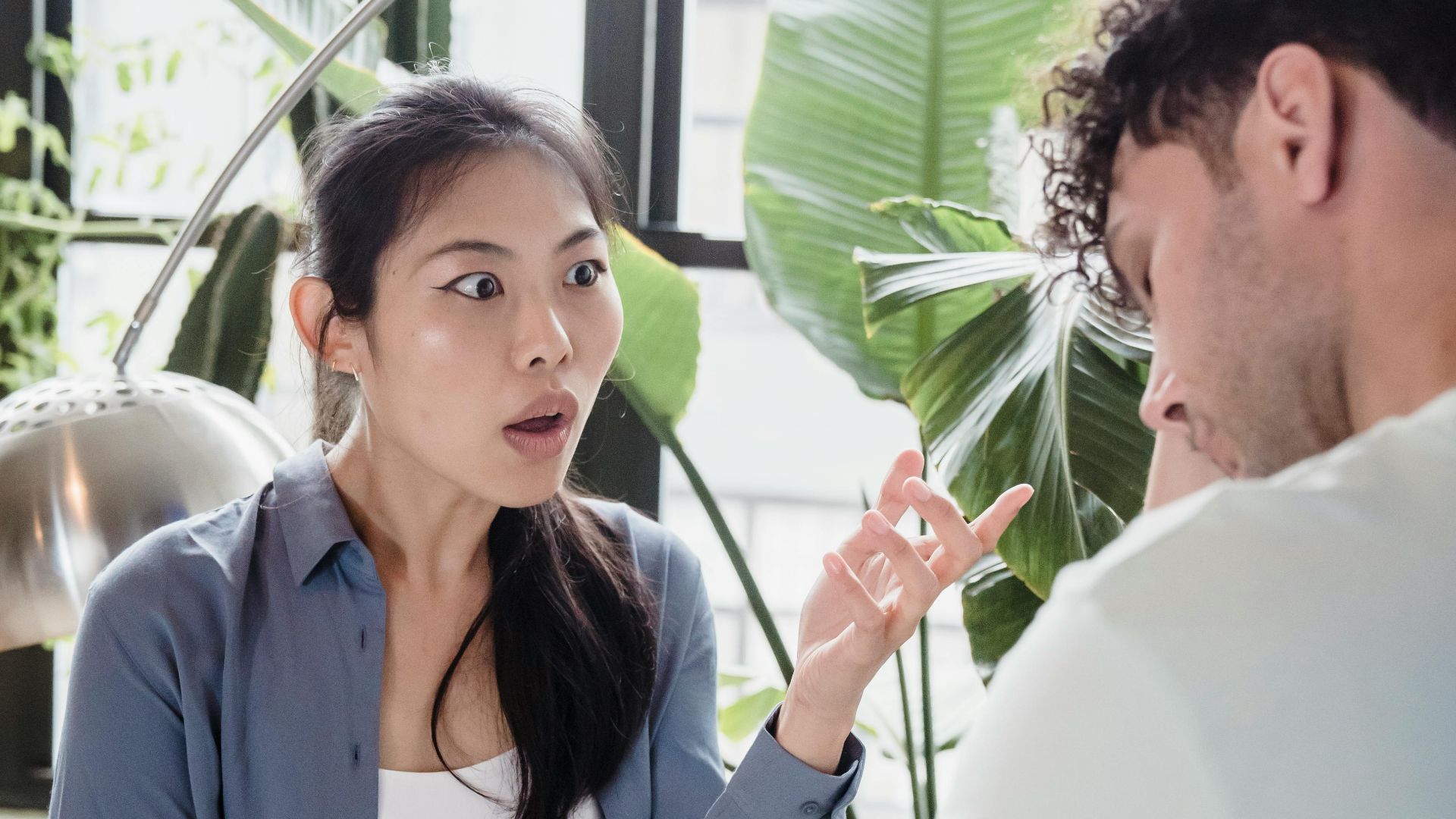 A couple engaged in a heated discussion in a room with lush indoor plants.