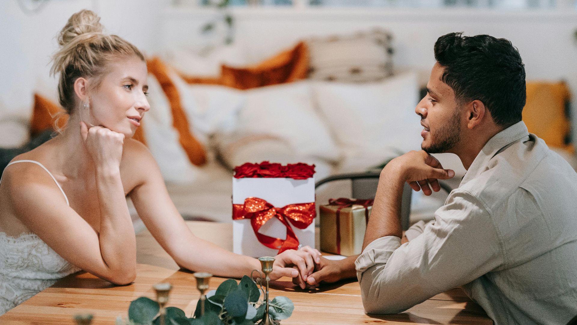 A loving couple enjoying a romantic date, holding hands indoors with a gift on the table.