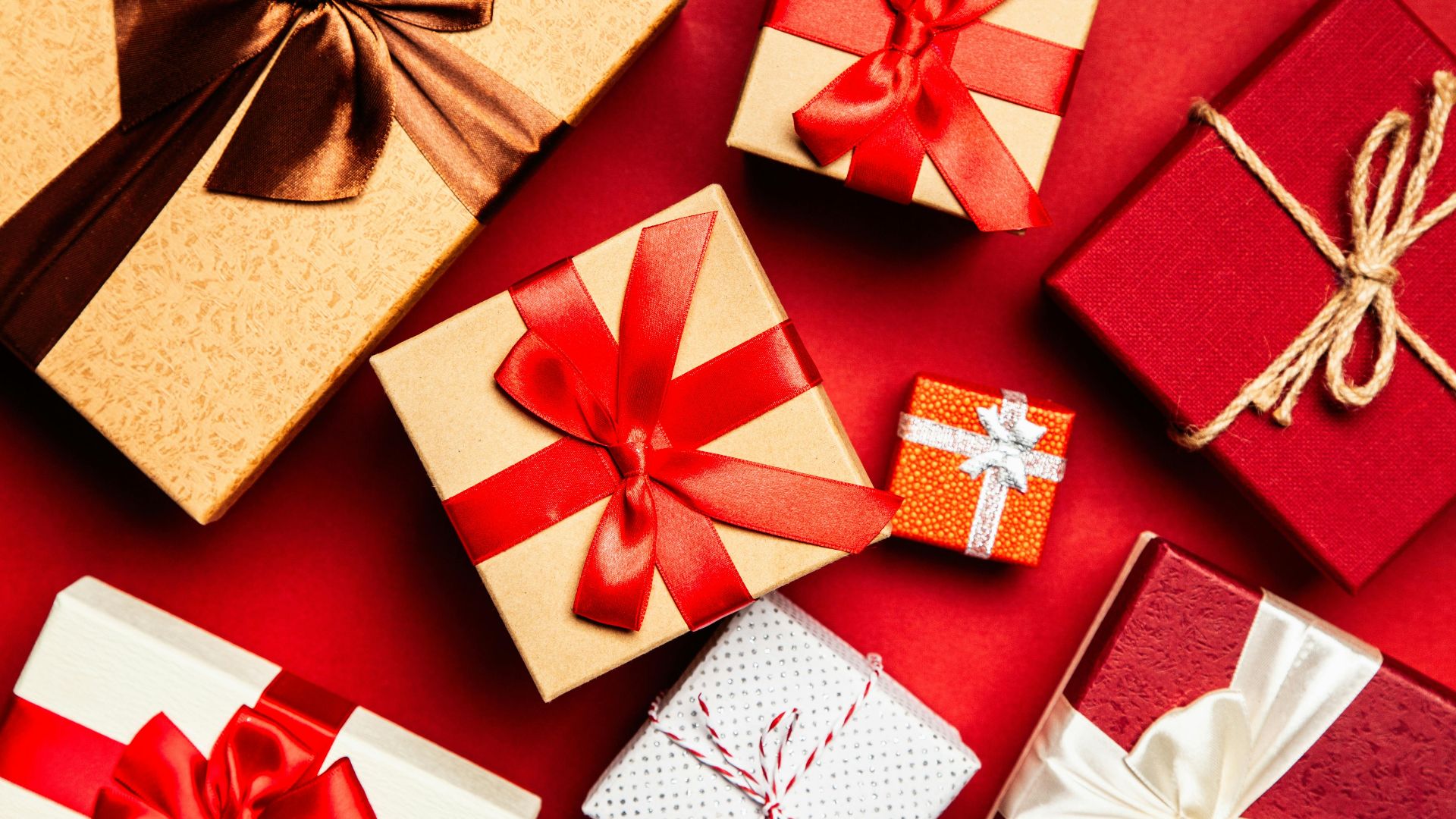 Top view of beautifully wrapped holiday gifts with red and brown ribbons on a vibrant red background.