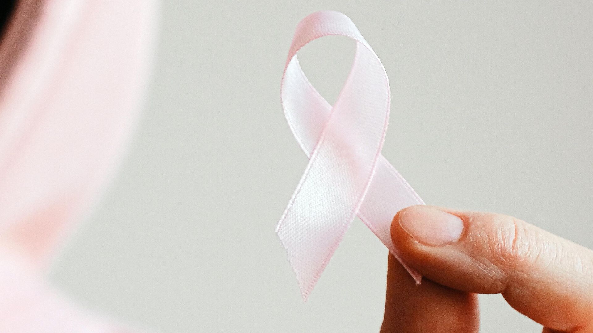 Close-up of a person holding a pink ribbon symbolizing breast cancer awareness.