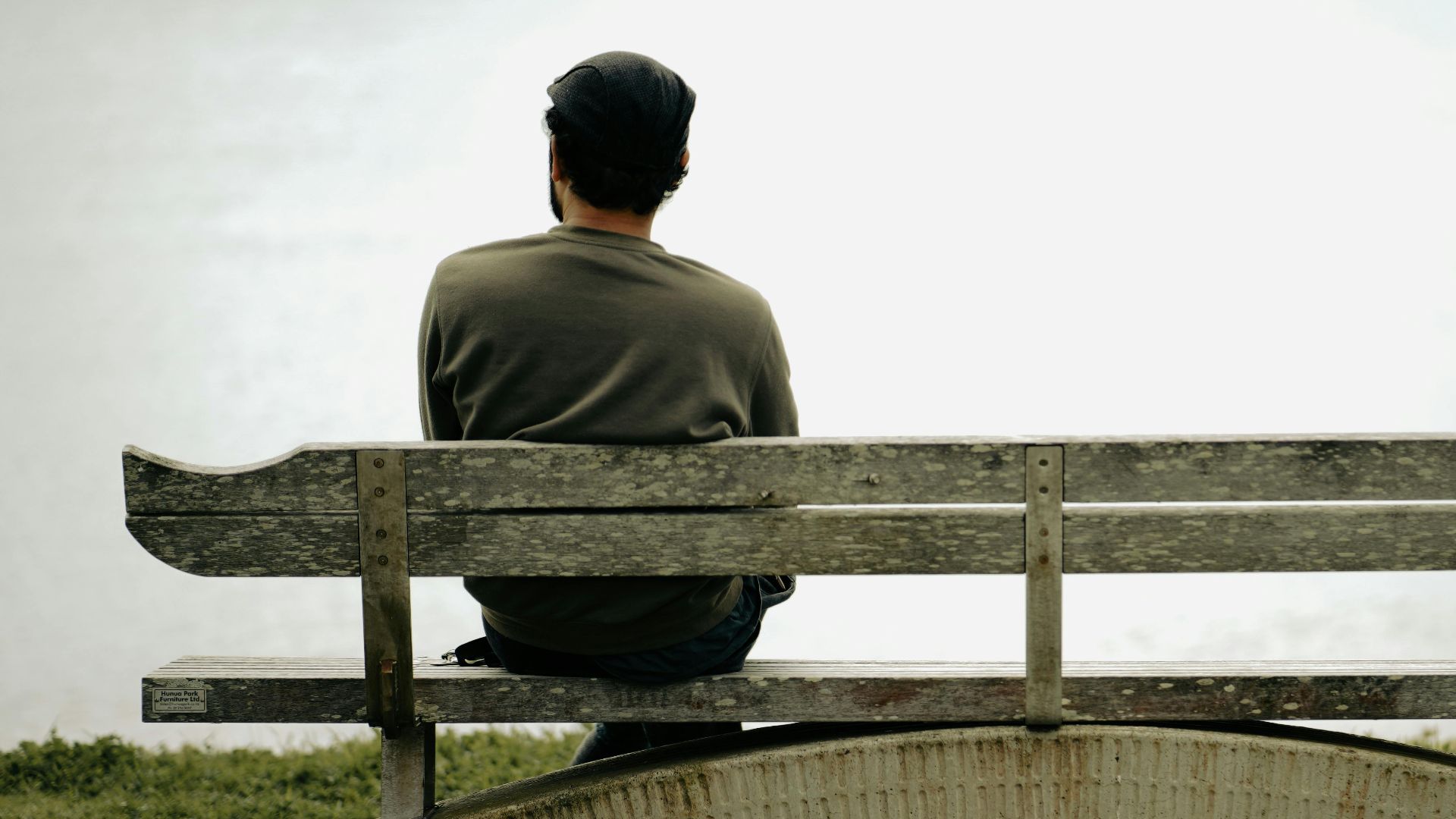 A person sits alone on a wooden bench by the water, capturing peaceful solitude.