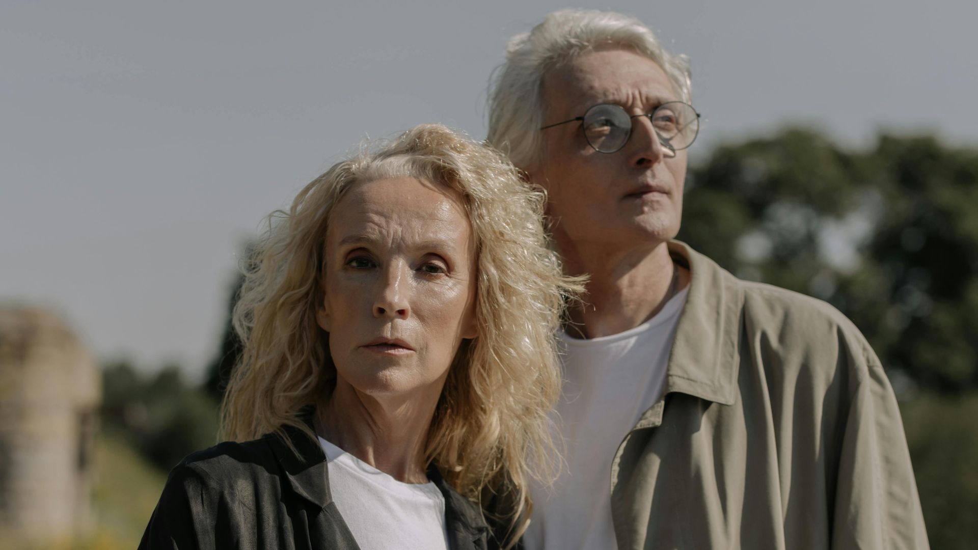 Elegant senior couple posing outdoors in stylish coats against a natural backdrop.