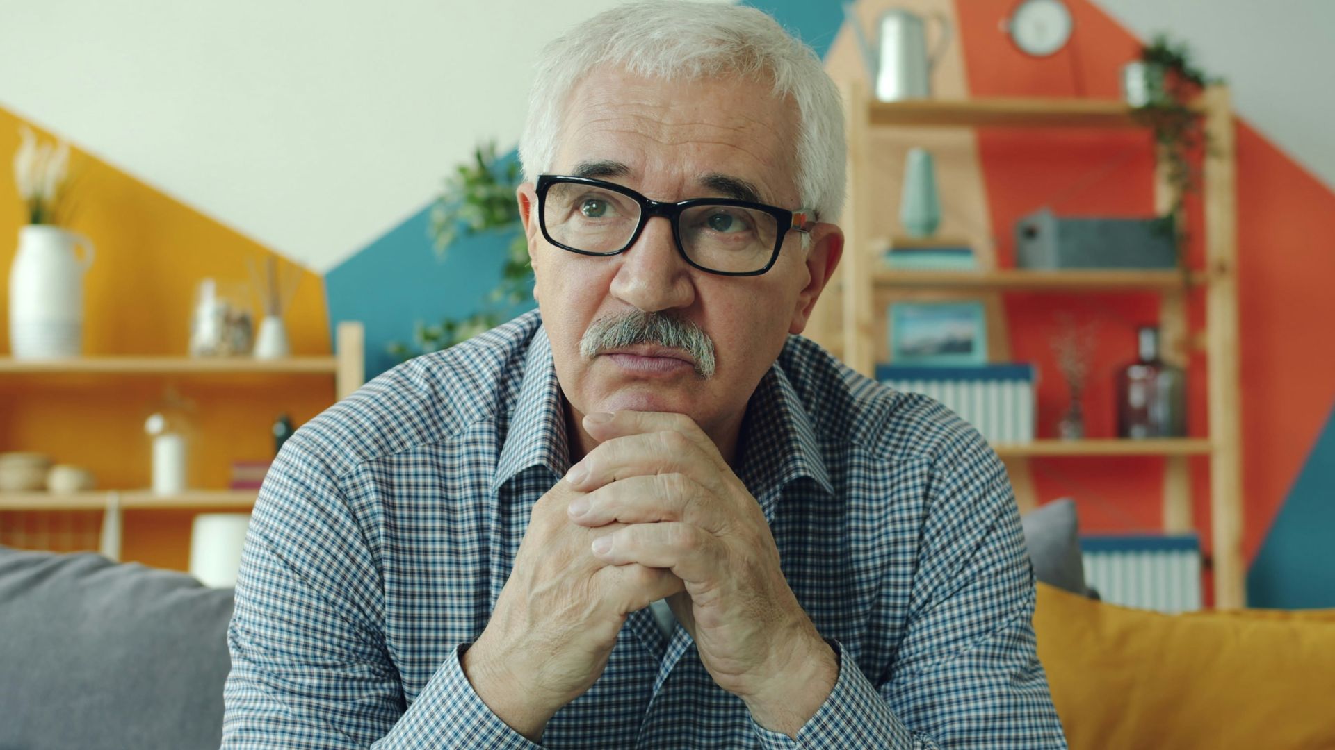 Elderly man with glasses resting chin on hands.