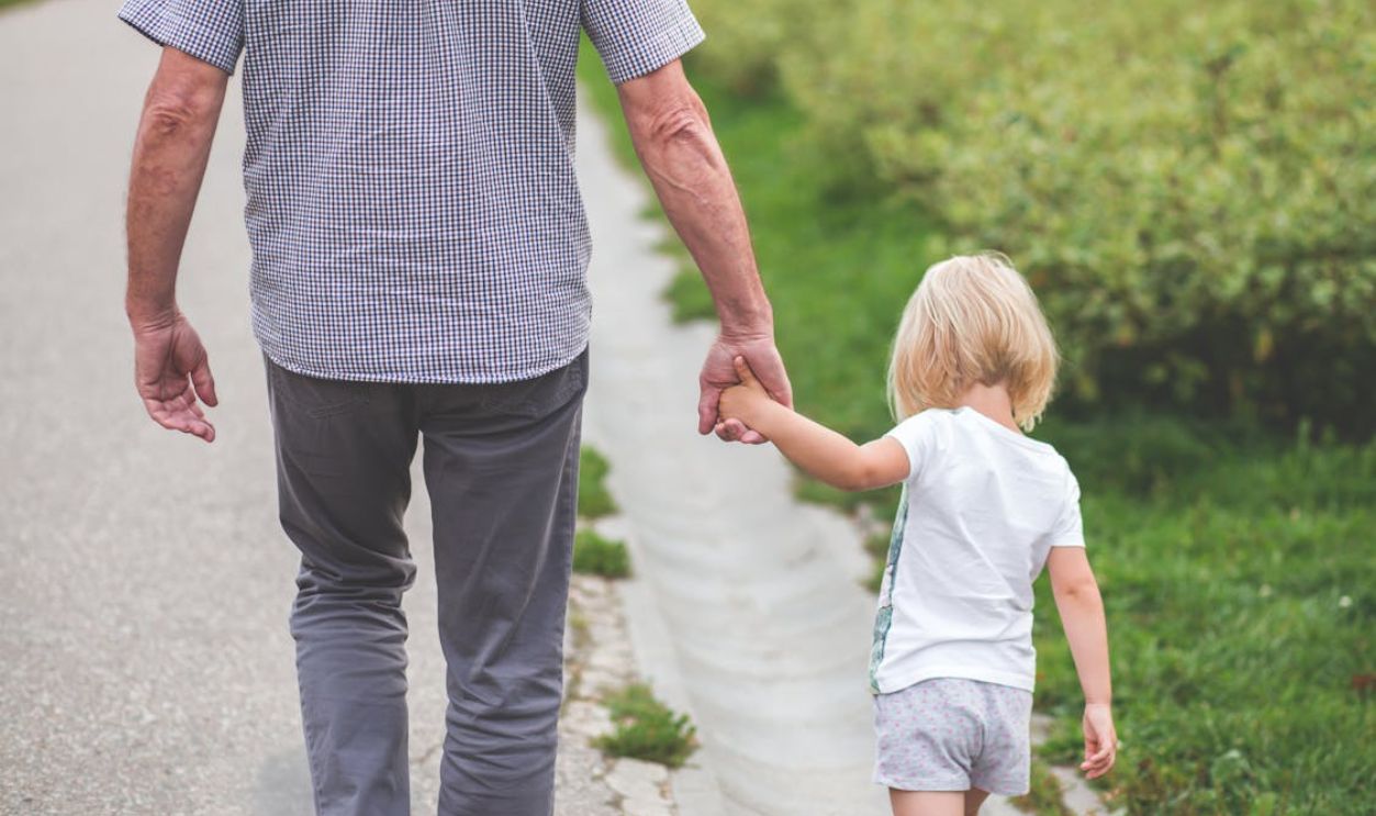 Man and Child Walking Near Bushes during Daytime
