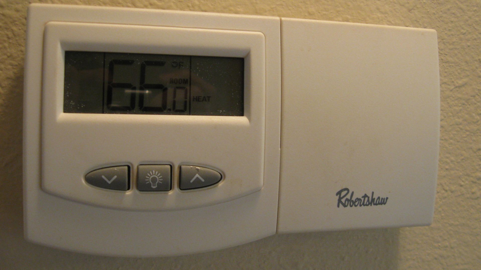 A Robertshaw non programmable digital thermostat with backlight controlling the central heating and cooling system of a house.