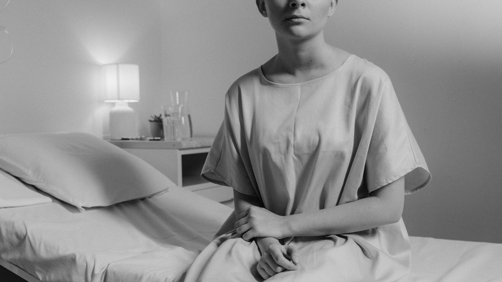 Black and white portrait of a young patient sitting on a hospital bed, conveying solitude and introspection.
